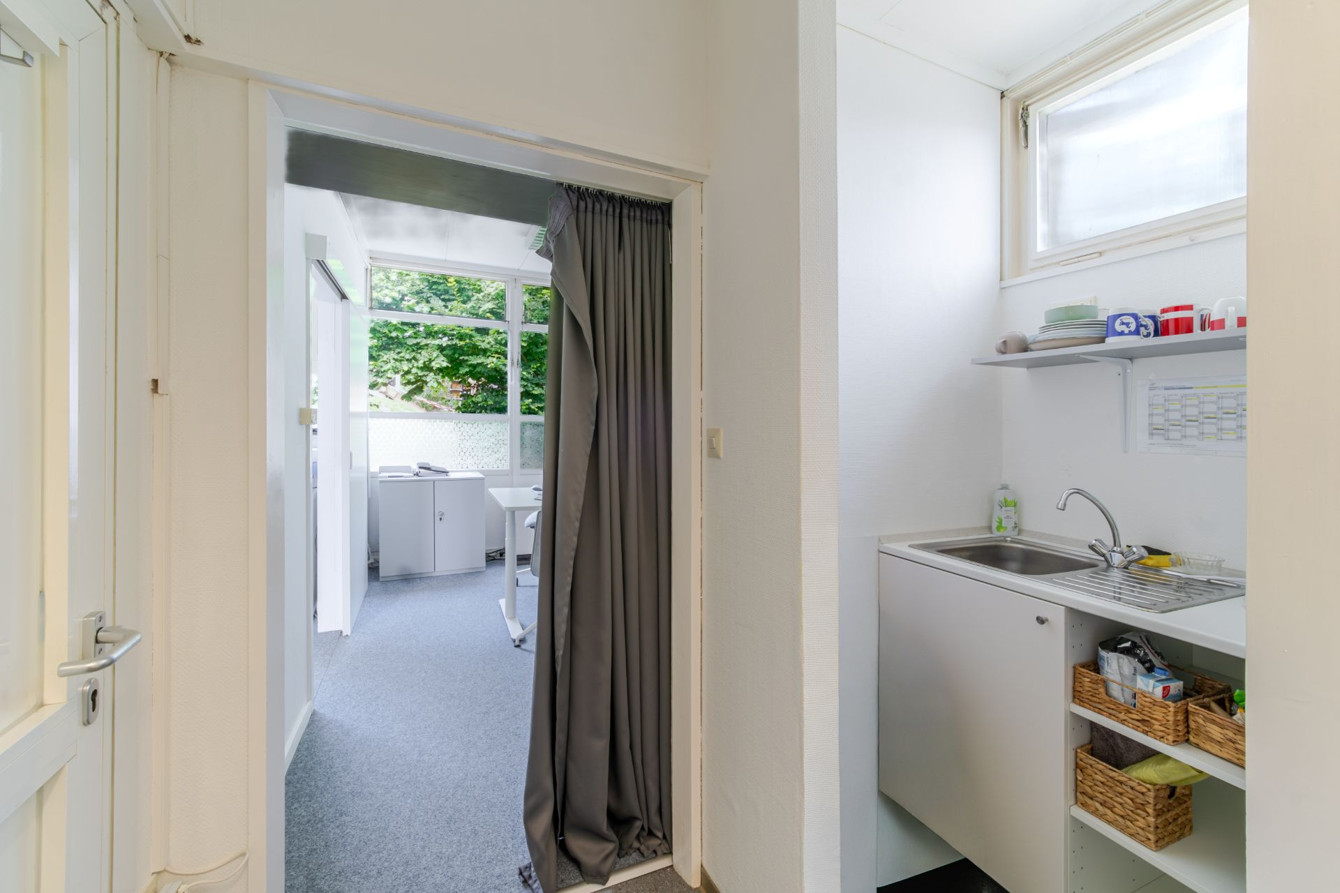Heller Flur mit Blick in ein Zimmer, rechts kleine Küchenzeile mit Regal und Spülbecken.