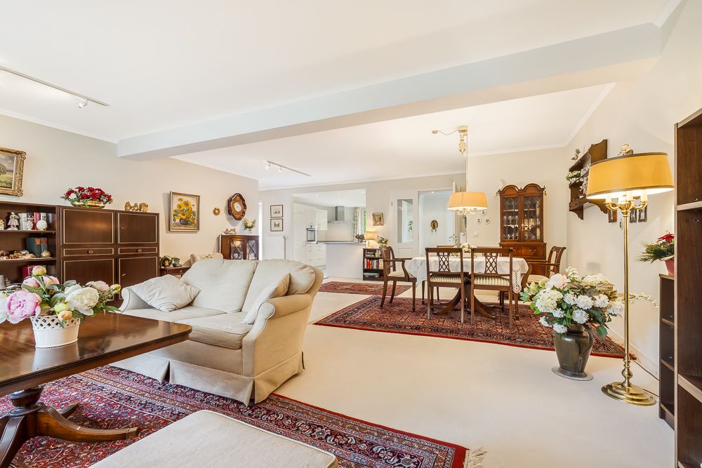 Helles Wohnzimmer mit Sofa, Esstisch, Teppichen und vielen Blumenarrangements.