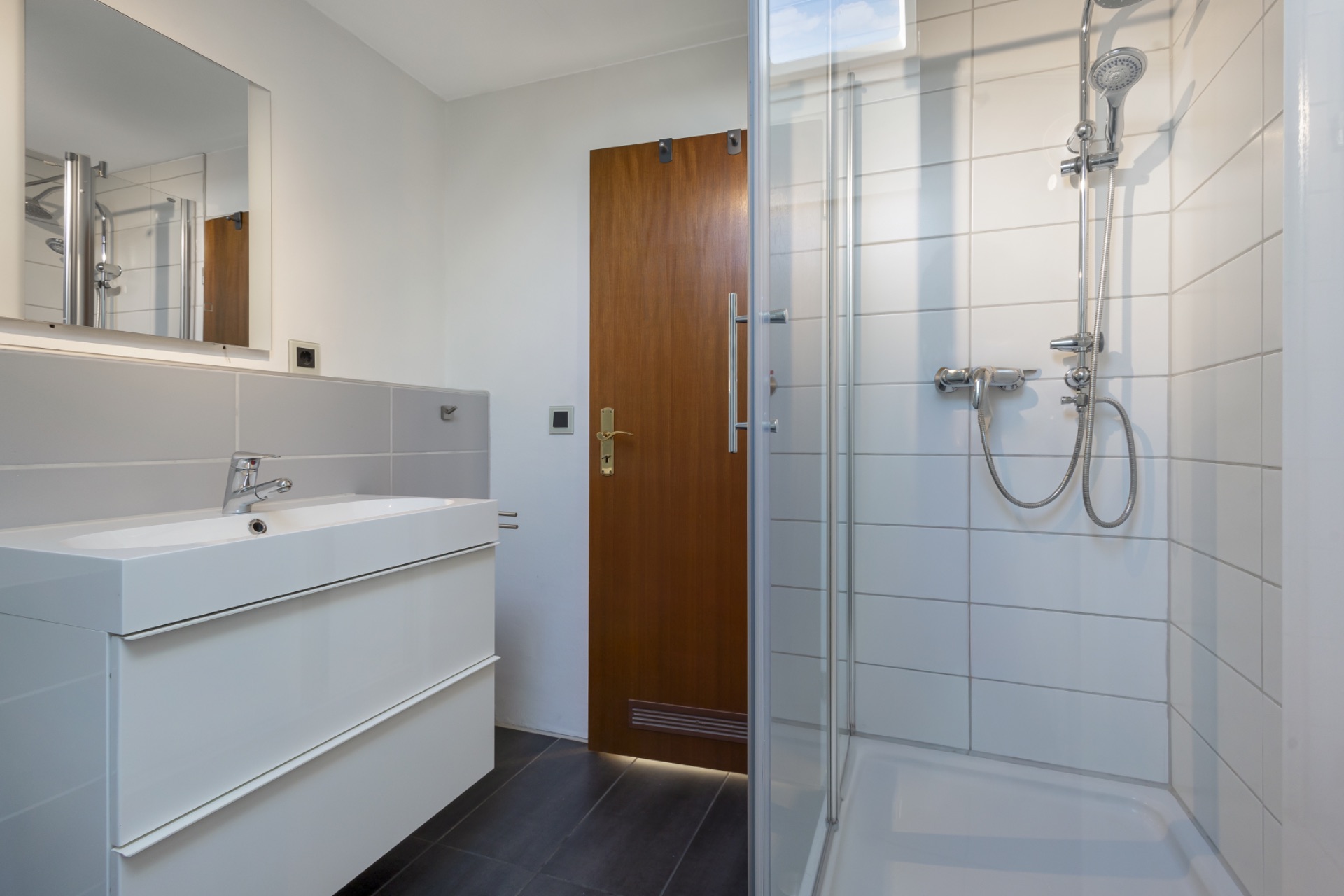 Modernes Badezimmer mit weißem Waschbecken, Spiegel und verglaster Dusche.