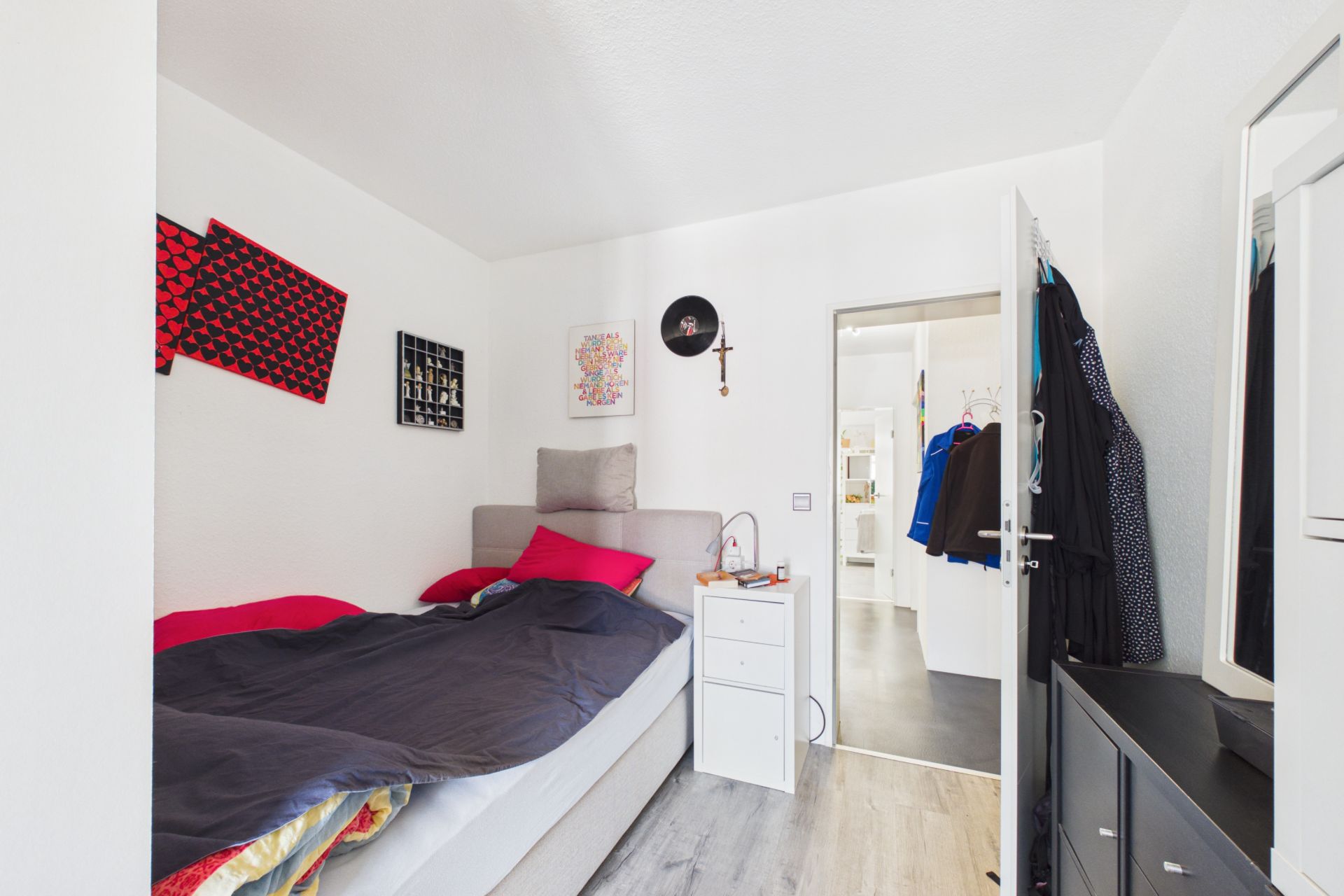 Kleines Schlafzimmer mit Bett, Nachttisch und Dekoration an den weißen Wänden.