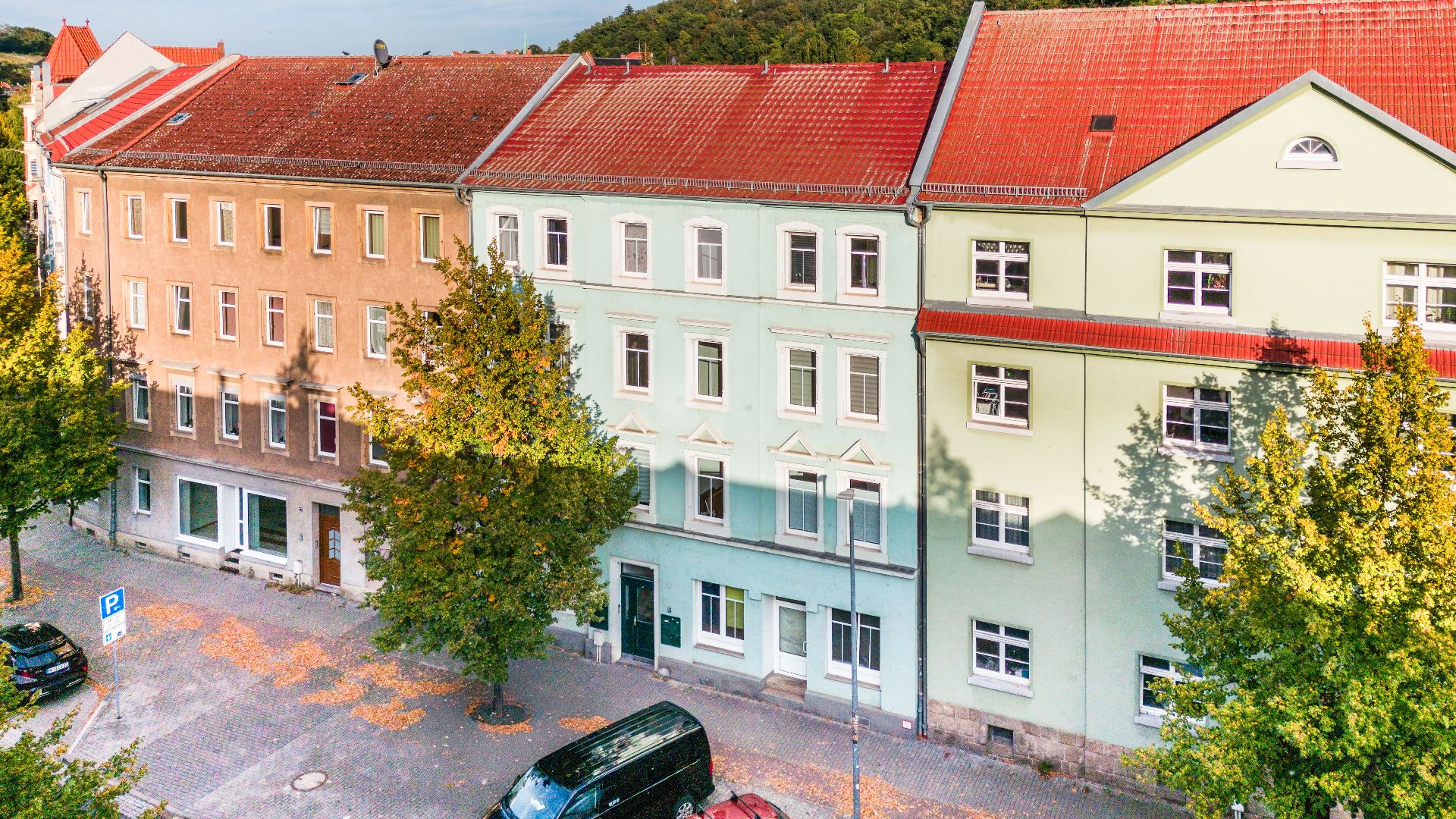 Mehrstöckige Wohnhäuser mit roten Dächern an einer von Bäumen gesäumten Straße.