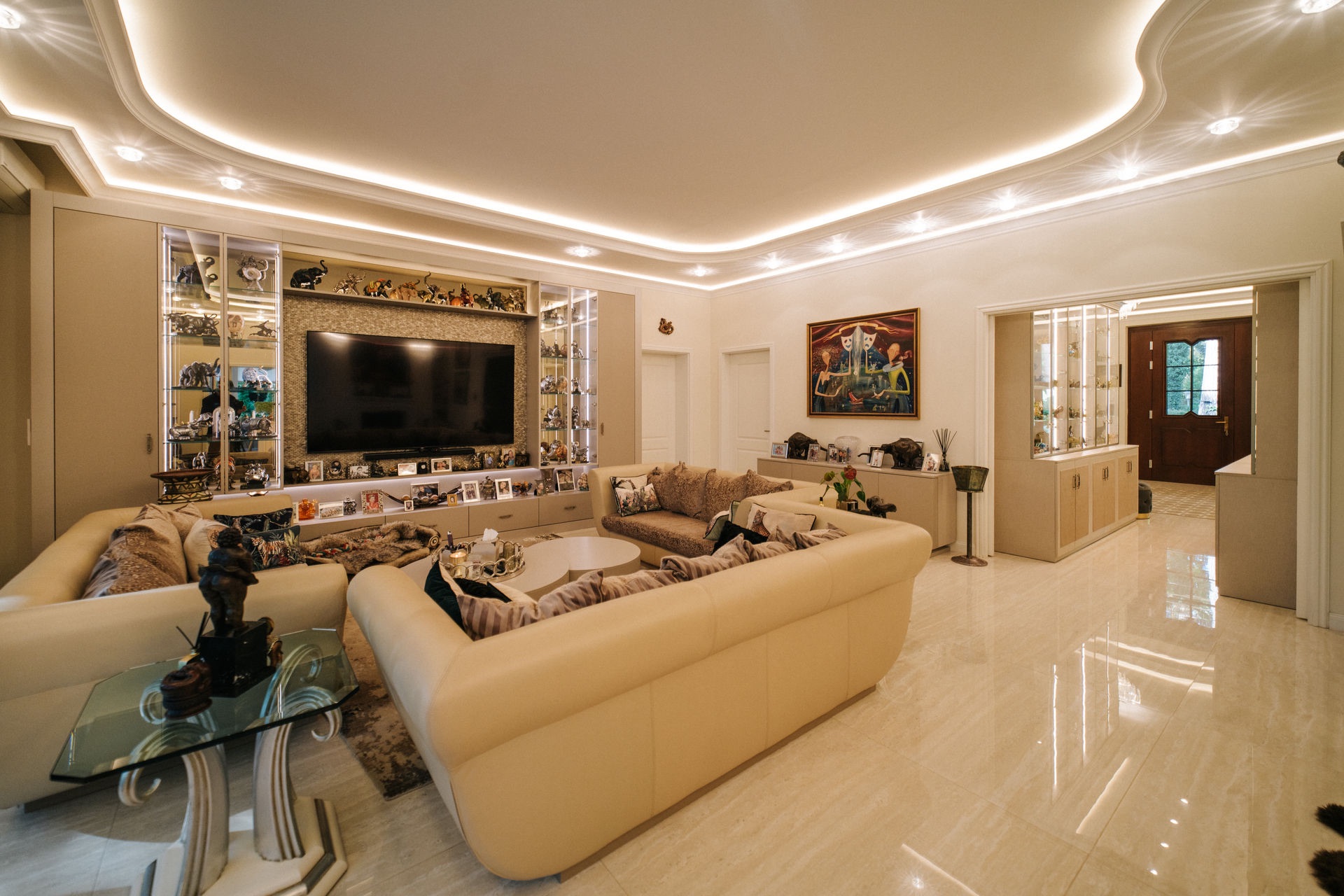 Modernes Wohnzimmer mit beigen Sofas, großem Fernseher und dekorativer Beleuchtung an der Decke.