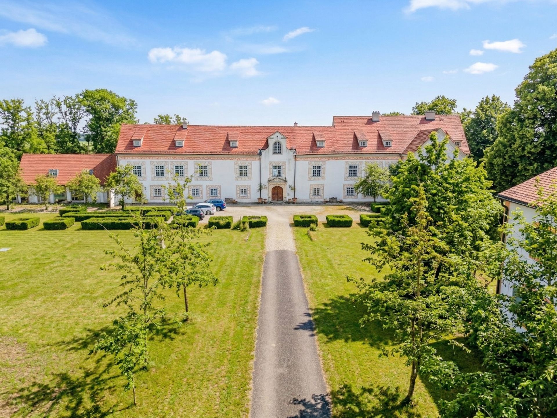 Großes, weißes Wohngebäude mit rotem Dach, von Garten und Bäumen umgeben.