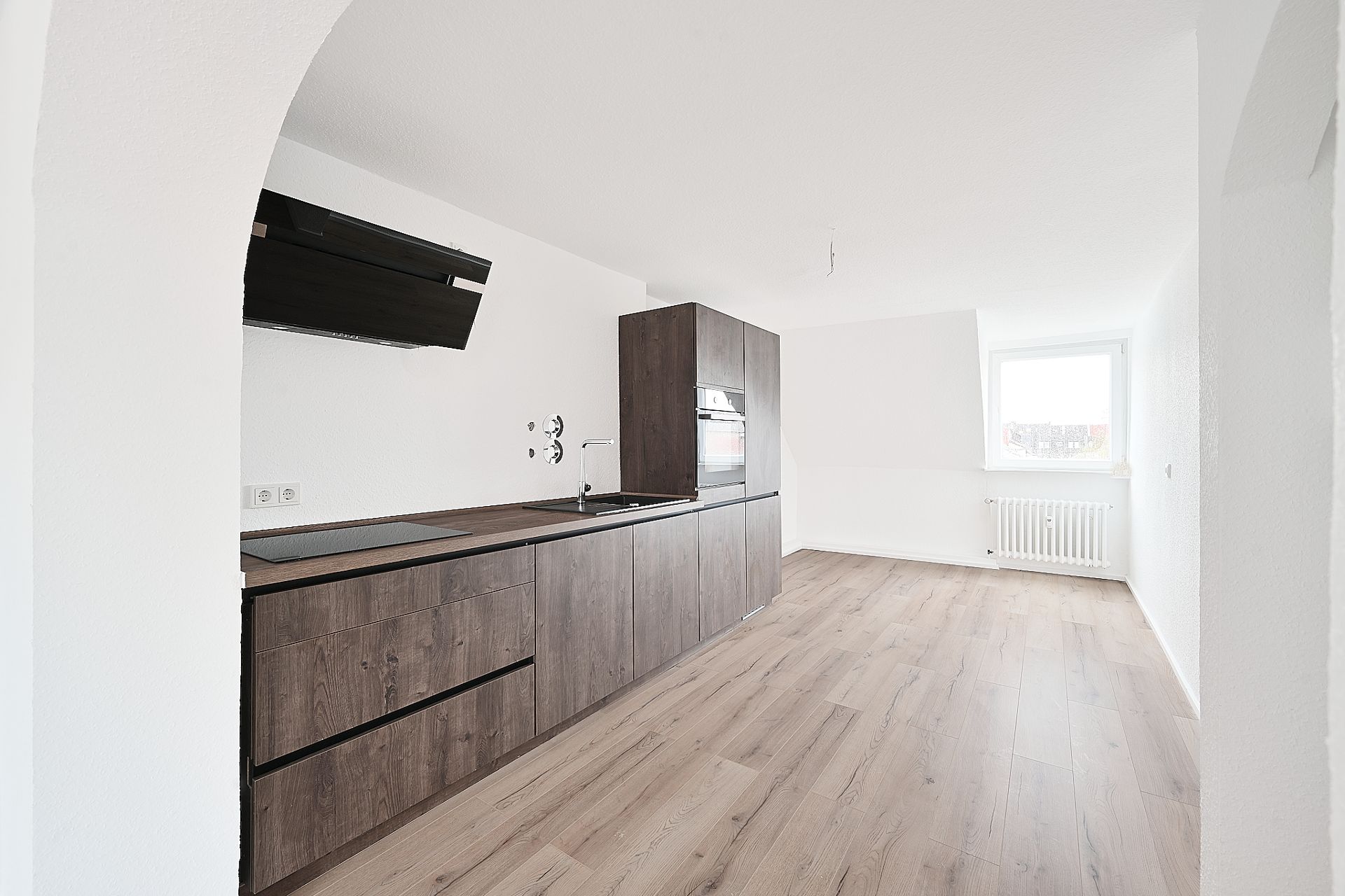 Helle Küche mit dunklen Holzmöbeln, offenem Raum und großem Fenster.