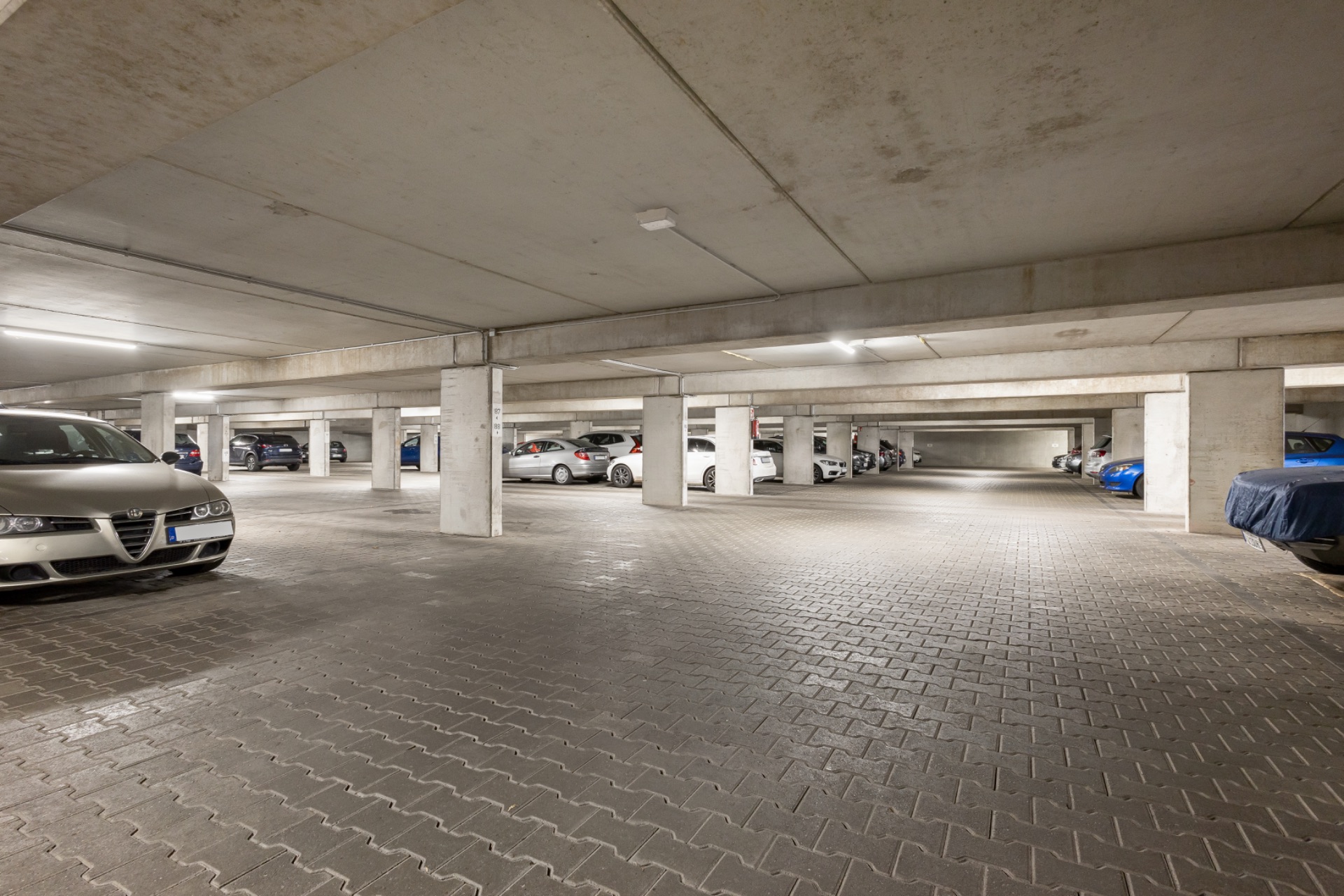 Große Tiefgarage mit parkenden Autos und Betonstützen.