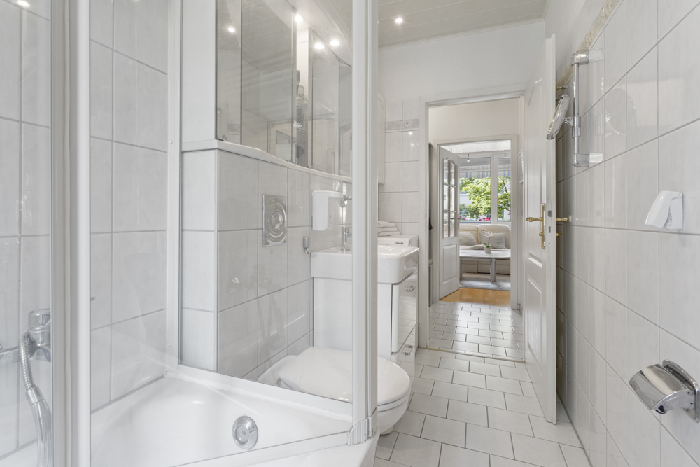 Helles Badezimmer mit Dusche, WC und Waschbecken, Blick ins Wohnzimmer.