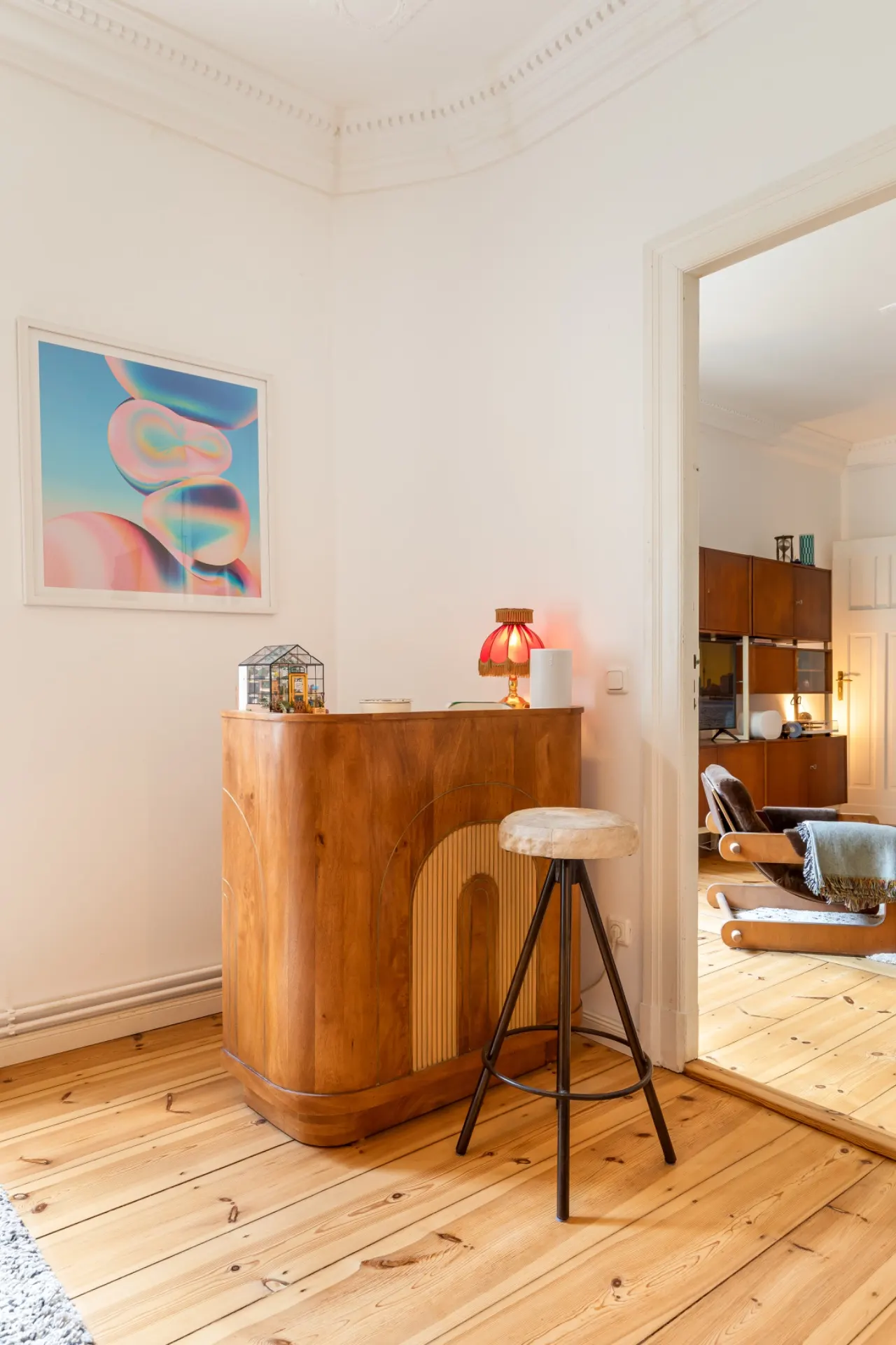 Ecke mit Holztheke, Hocker, bunter Lampe und abstraktem Bild an weißer Wand in einer Wohnung.