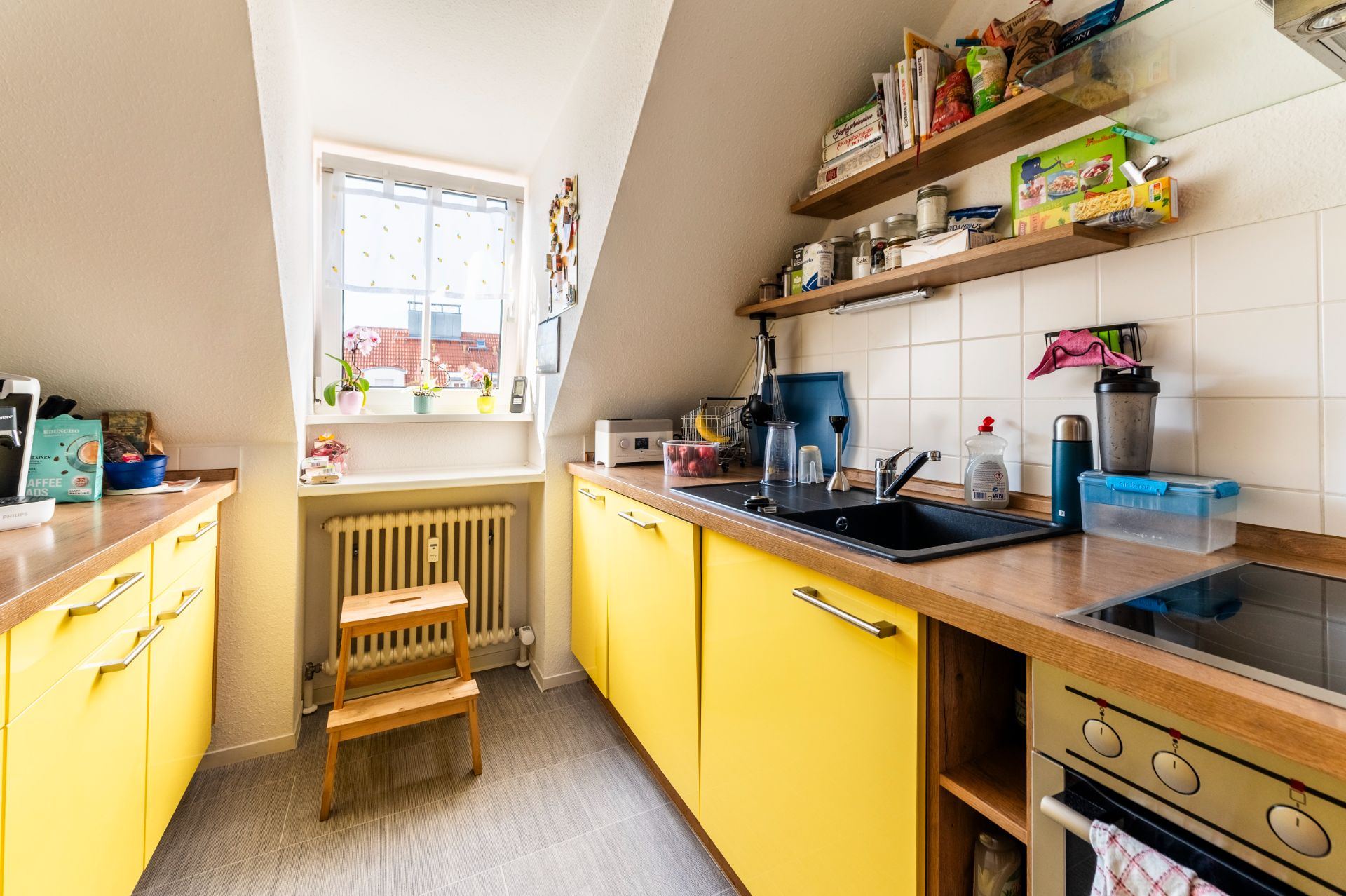 Schmale Küche mit gelben Schränken, Holzarbeitsplatte und Fenster am Ende des Raums.