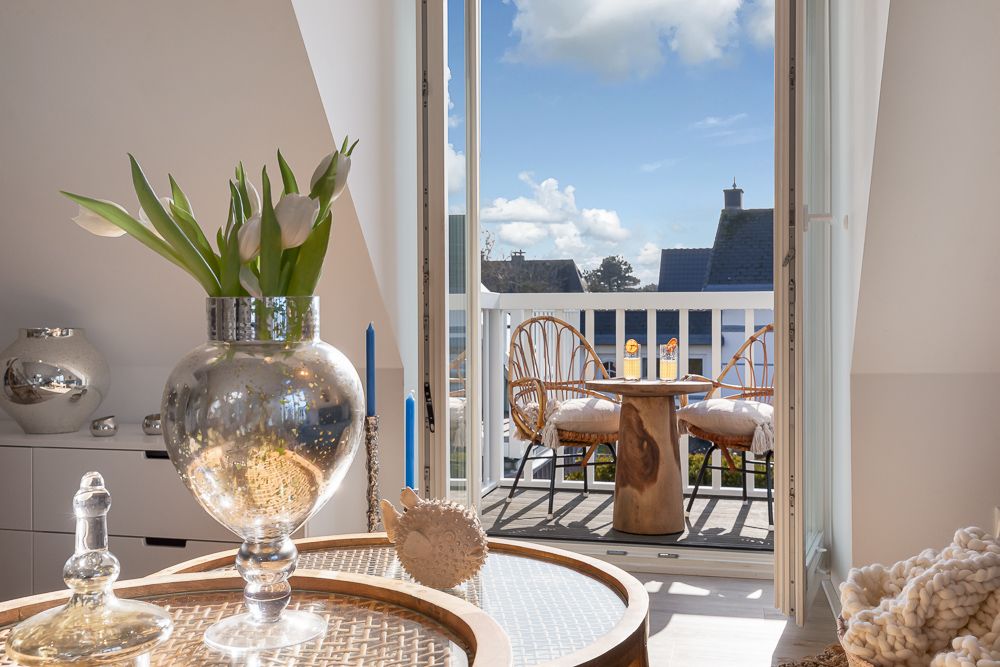 Wohnzimmer mit Glastisch, Vase mit Blumen und Zugang zu einem Balkon mit zwei Stühlen und Tisch.