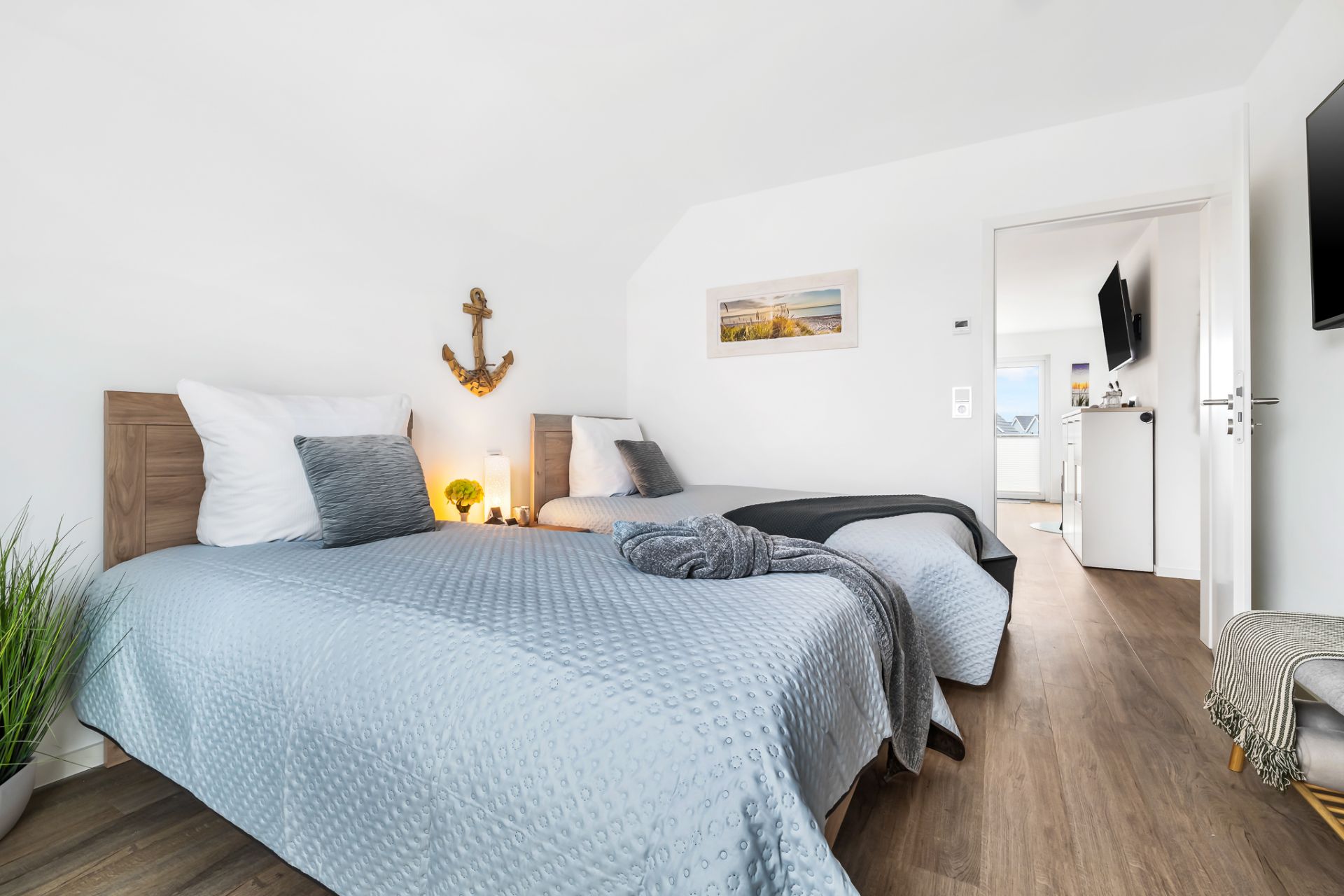 Schlafzimmer mit zwei Einzelbetten, Holzboden, Wanddeko und offenem Durchgang zum Flur.