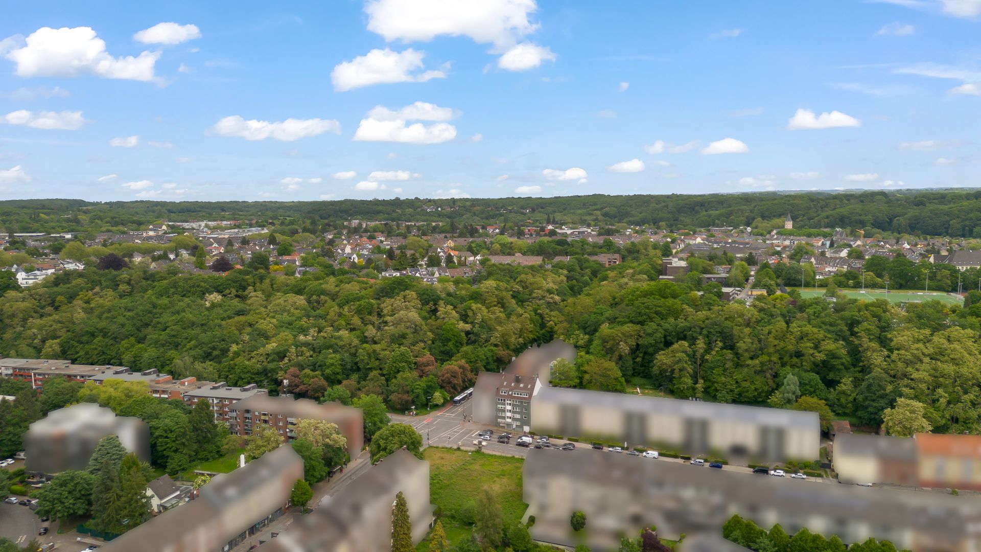 Blick auf eine Wohnsiedlung mit vielen Bäumen und Häusern an einer Straße bei Tageslicht.