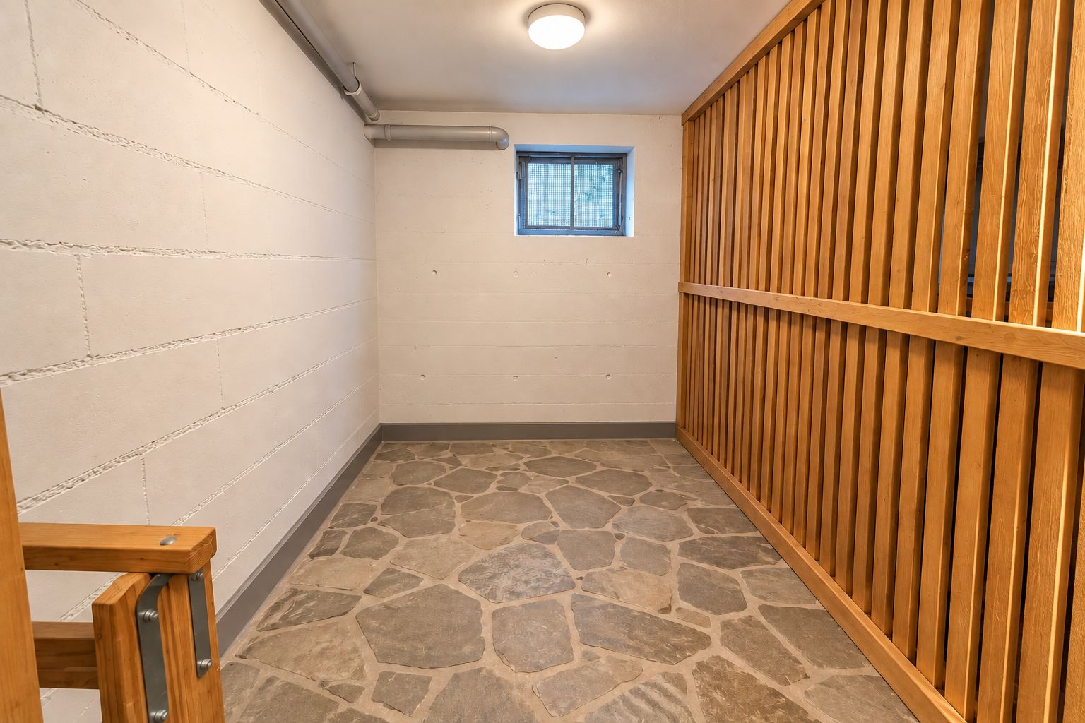 Kleiner Kellerraum mit Steinboden, weißer Wand und Holzabtrennung, kleines Fenster an der Rückwand.