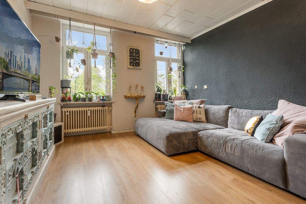 Wohnzimmer mit grauem Sofa, Holzboden, Pflanzen am Fenster und Wanddekoration.
