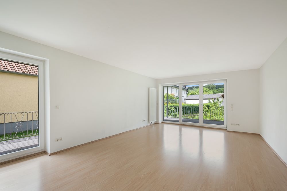 Helles, leeres Wohnzimmer mit Parkettboden und großen Fenstern, Blick auf Garten und Terrasse.