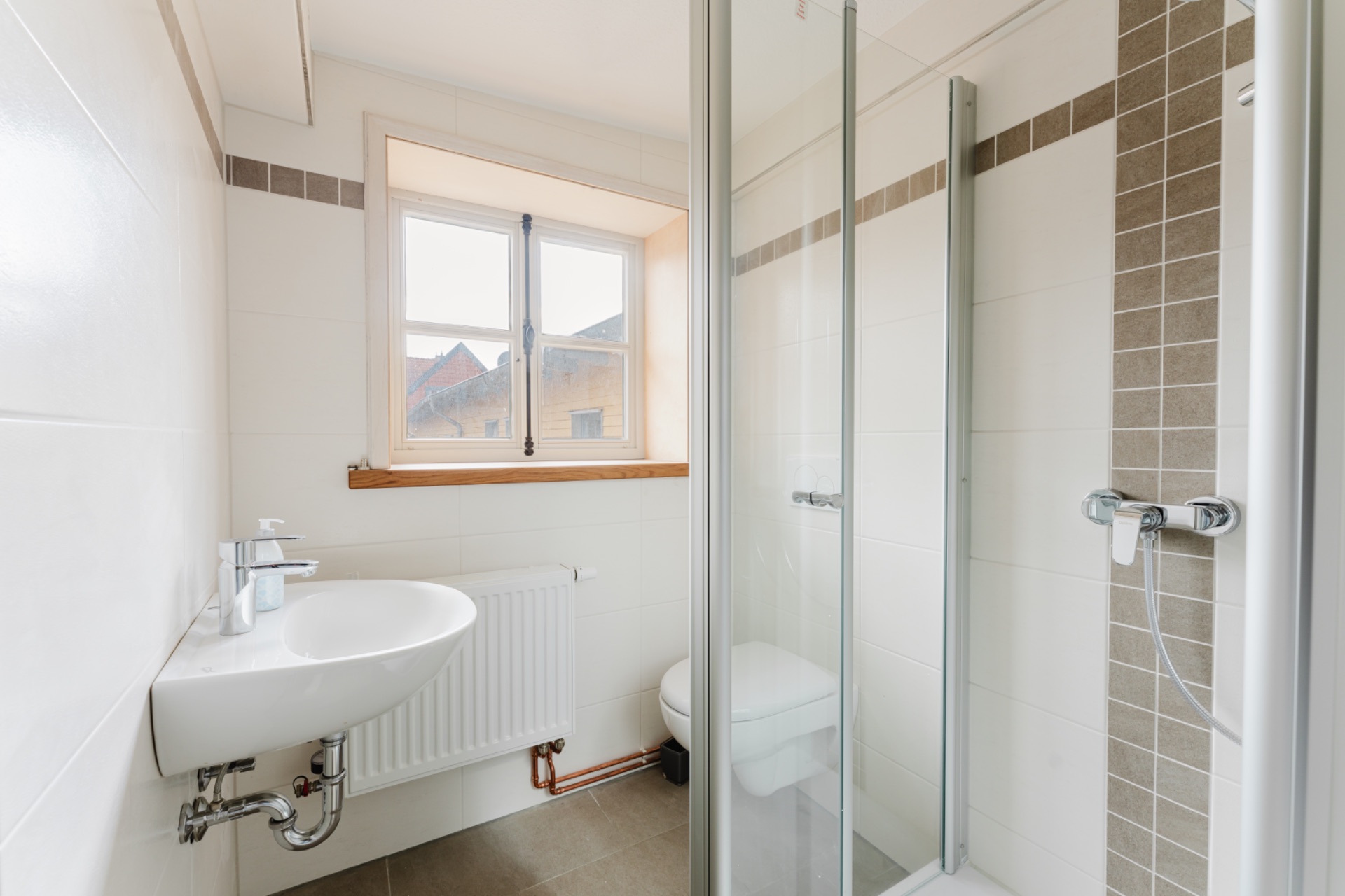 Kleines, helles Badezimmer mit Waschbecken, Dusche, Toilette und Fenster.