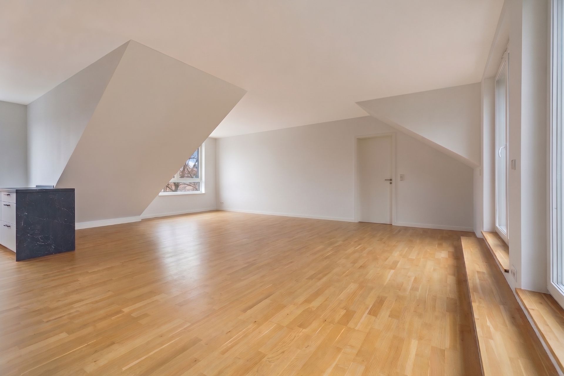Leerer Raum mit Holzfußboden, weißen Wänden und großen Fenstern, schräge Decke.
