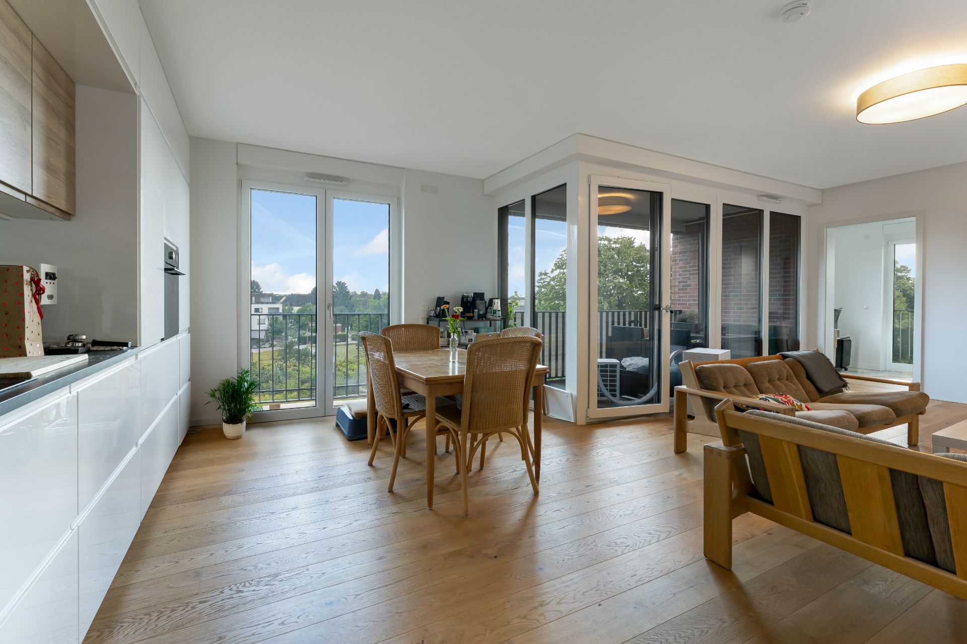 Helles Wohnzimmer mit Holzboden, Esstisch, Sofa und verglaster Loggia, Blick nach draußen.