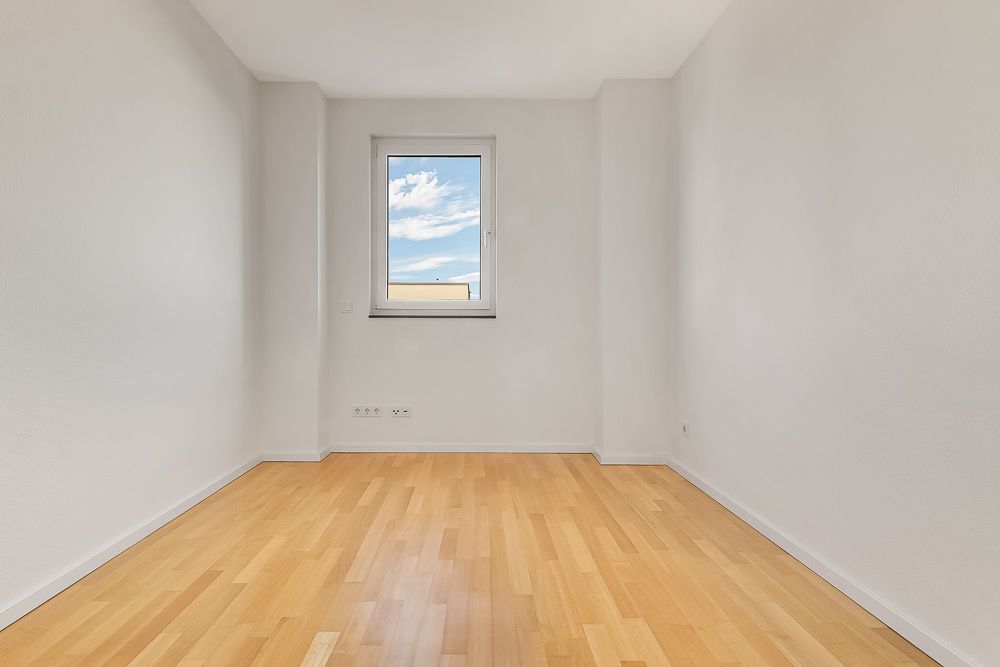 Leerer Raum mit hellem Holzboden und einem Fenster in der Mitte der Rückwand.