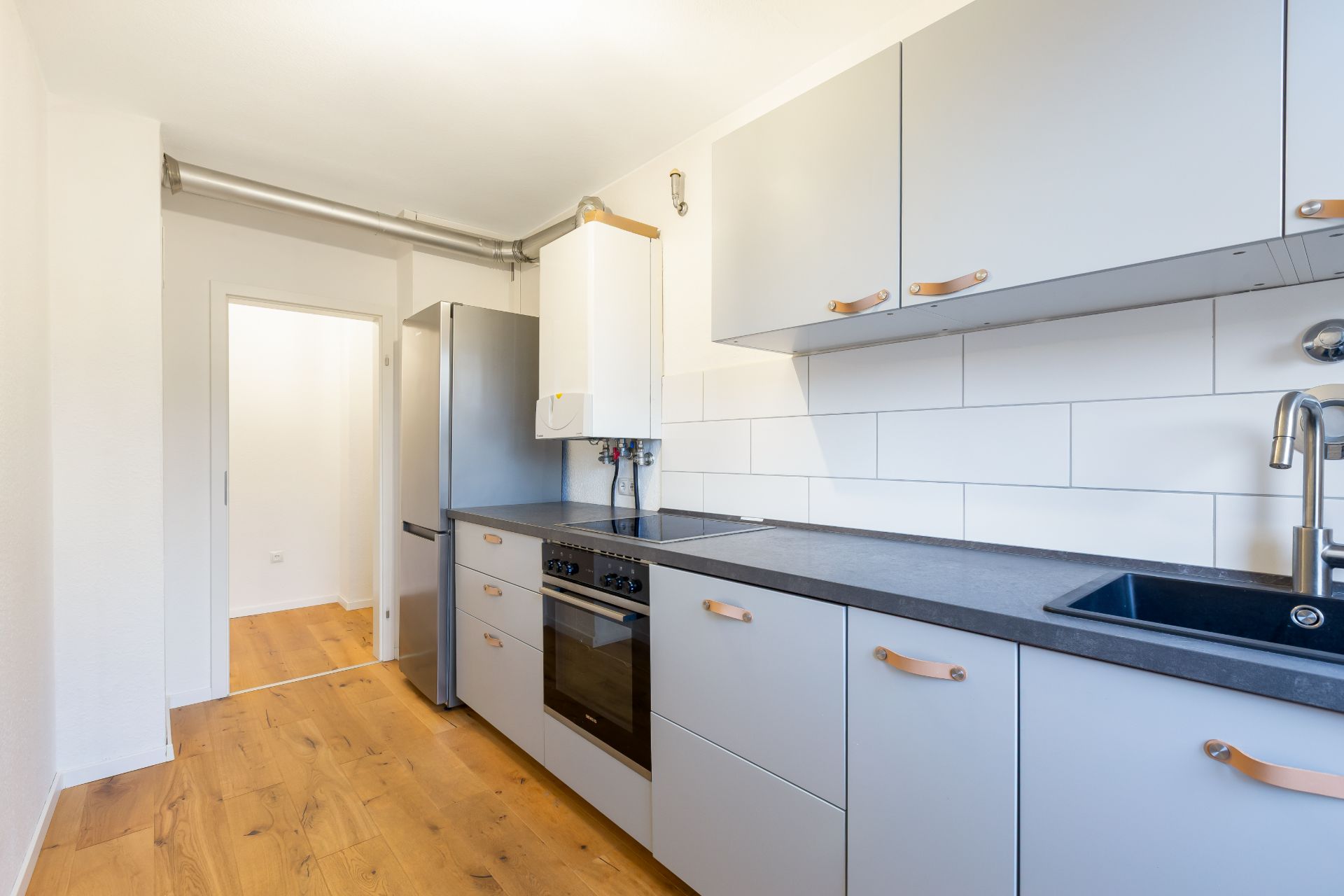 Moderne Küche mit grauen Schränken, Holzfußboden, Ofen, Kühlschrank und Spüle.