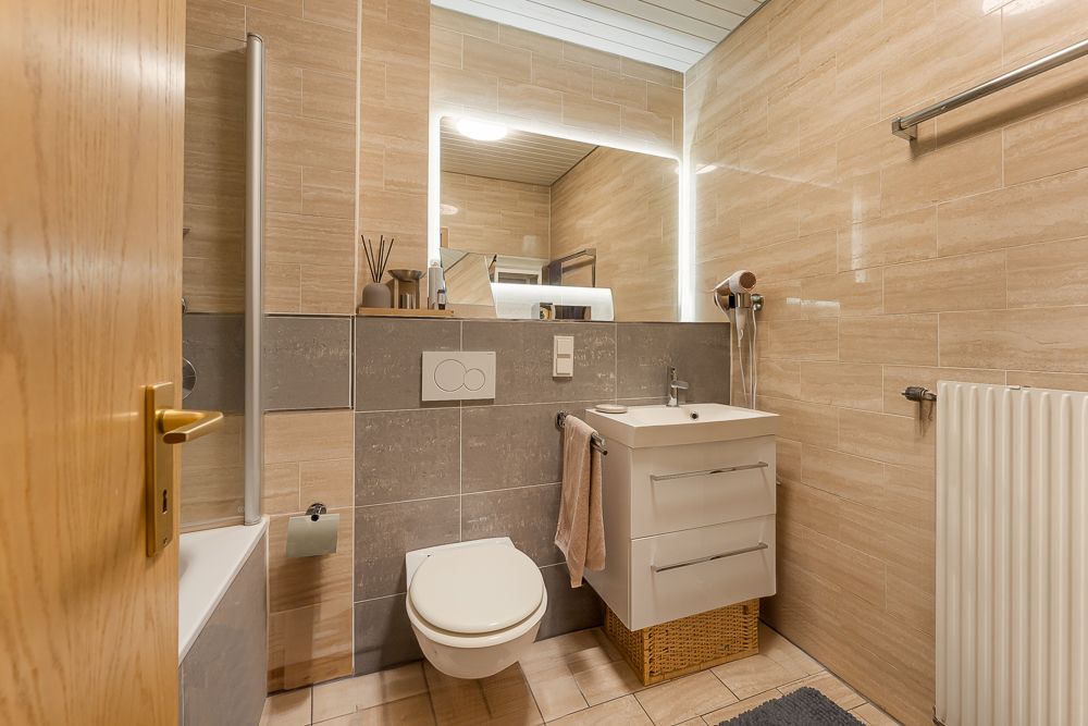 Modernes Badezimmer mit Wandtoilette, Waschbecken, großem Spiegel und Handtuchheizkörper.