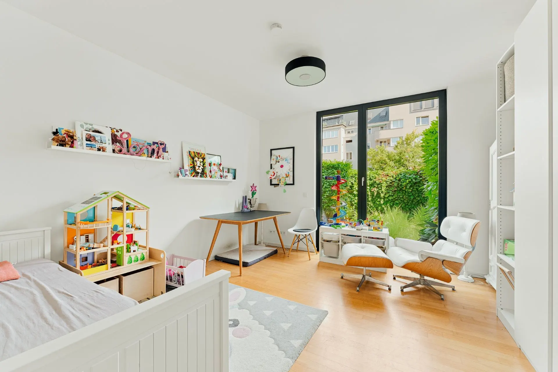 Helles Kinderzimmer mit Spielzeug, Bett, Schreibtisch und großem Fenster zum Garten.