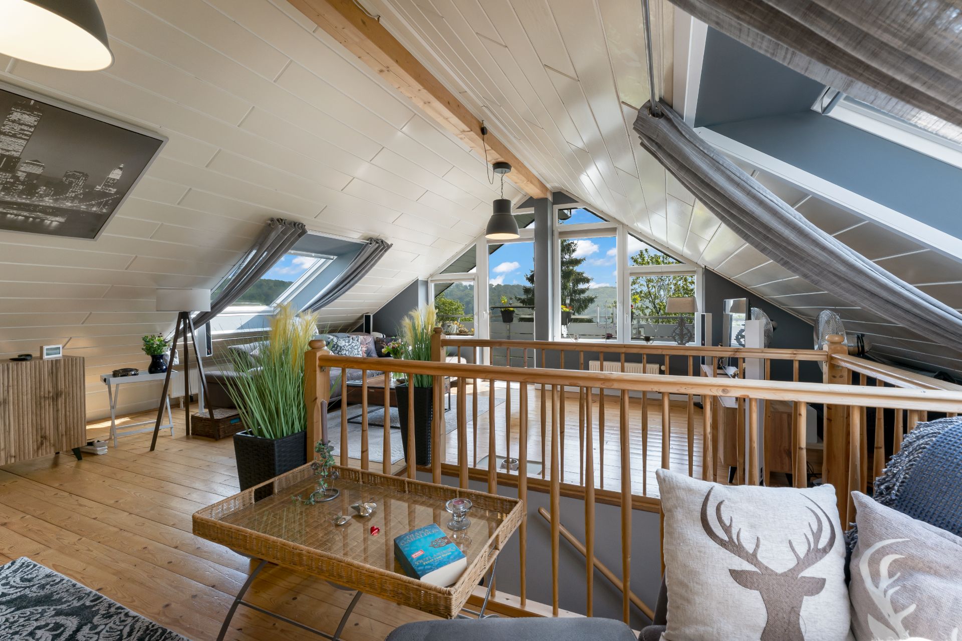 Modernes Wohnzimmer im Dachgeschoss mit Holzboden, Sofa, Pflanzen und großen Fenstern.