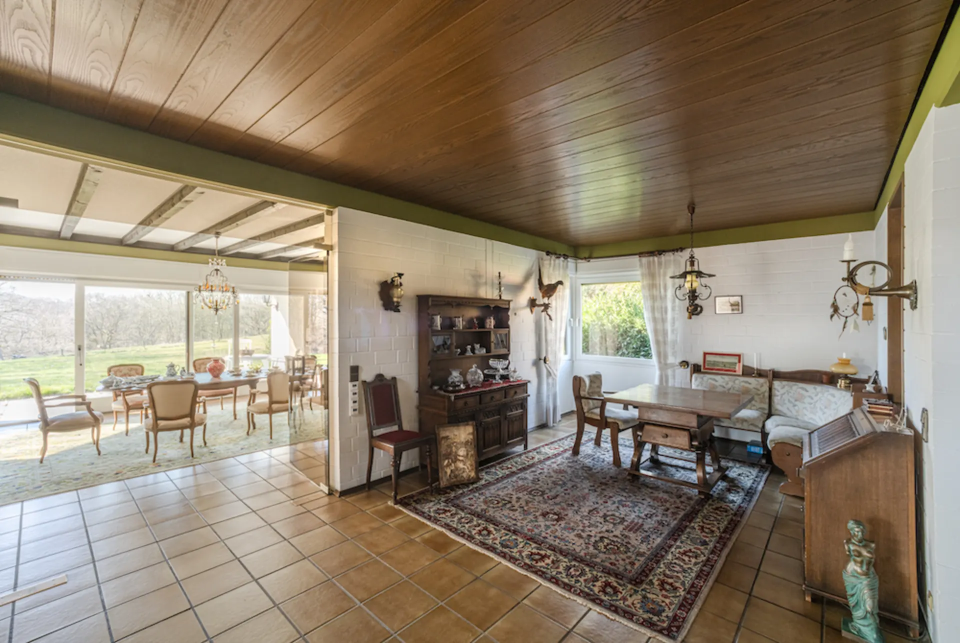 Wohnzimmer mit Holzboden, Teppich, antiken Möbeln und Blick in ein helles Esszimmer mit großen Fenstern.
