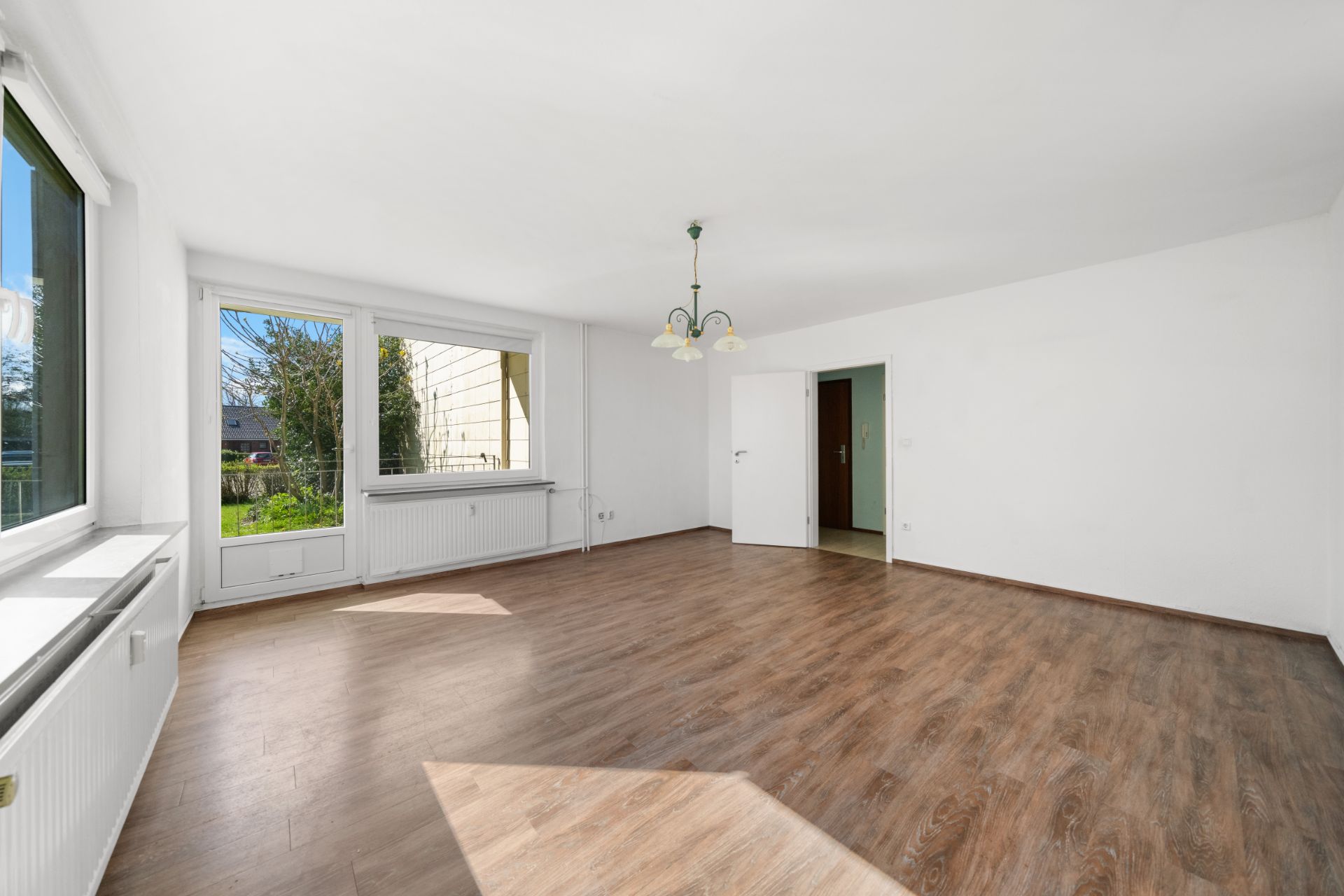 Leeres Wohnzimmer mit großen Fenstern, Holzboden und einer Deckenlampe.