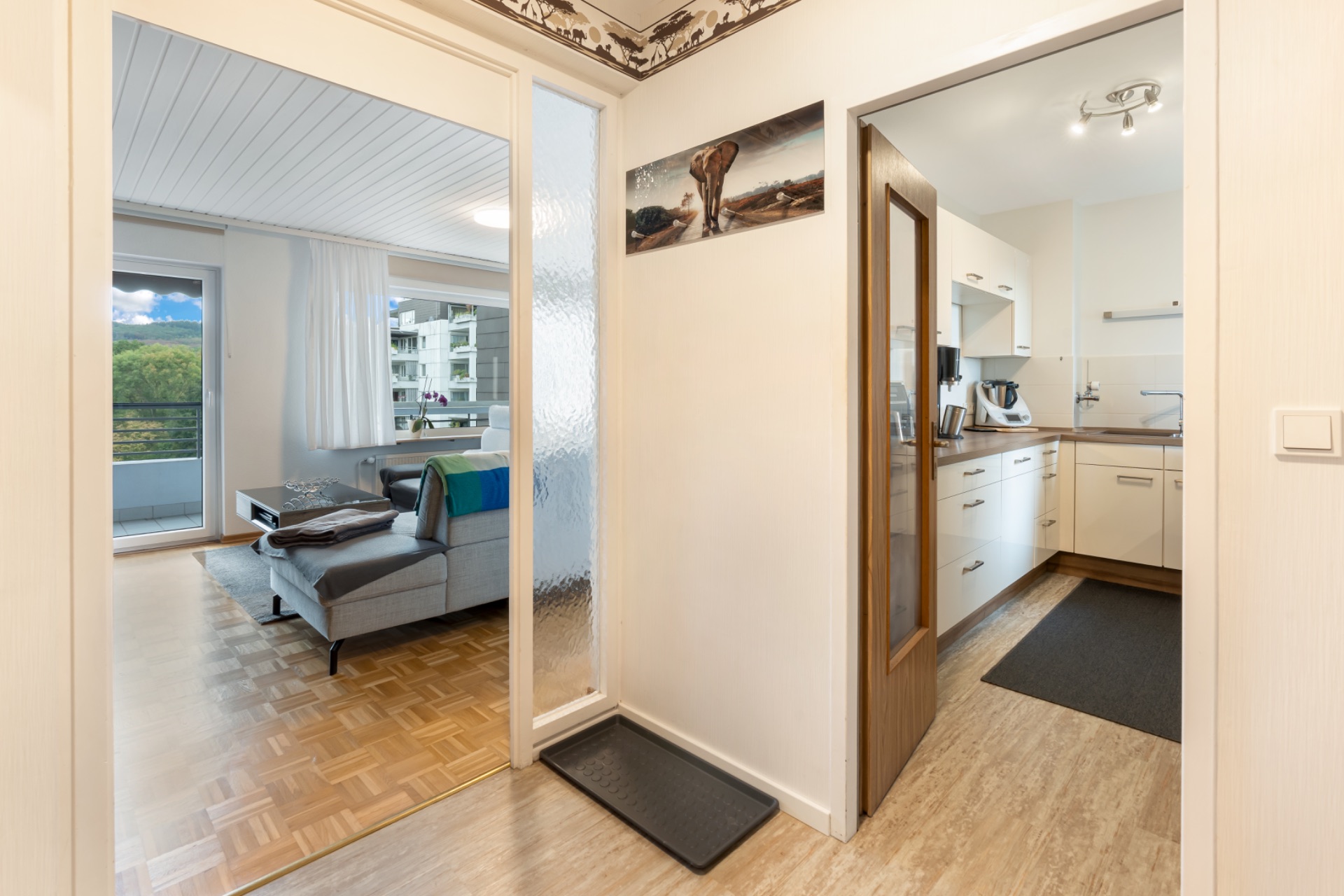 Flur mit Blick ins Wohnzimmer mit Sofa und in eine helle Küche mit Holzboden.