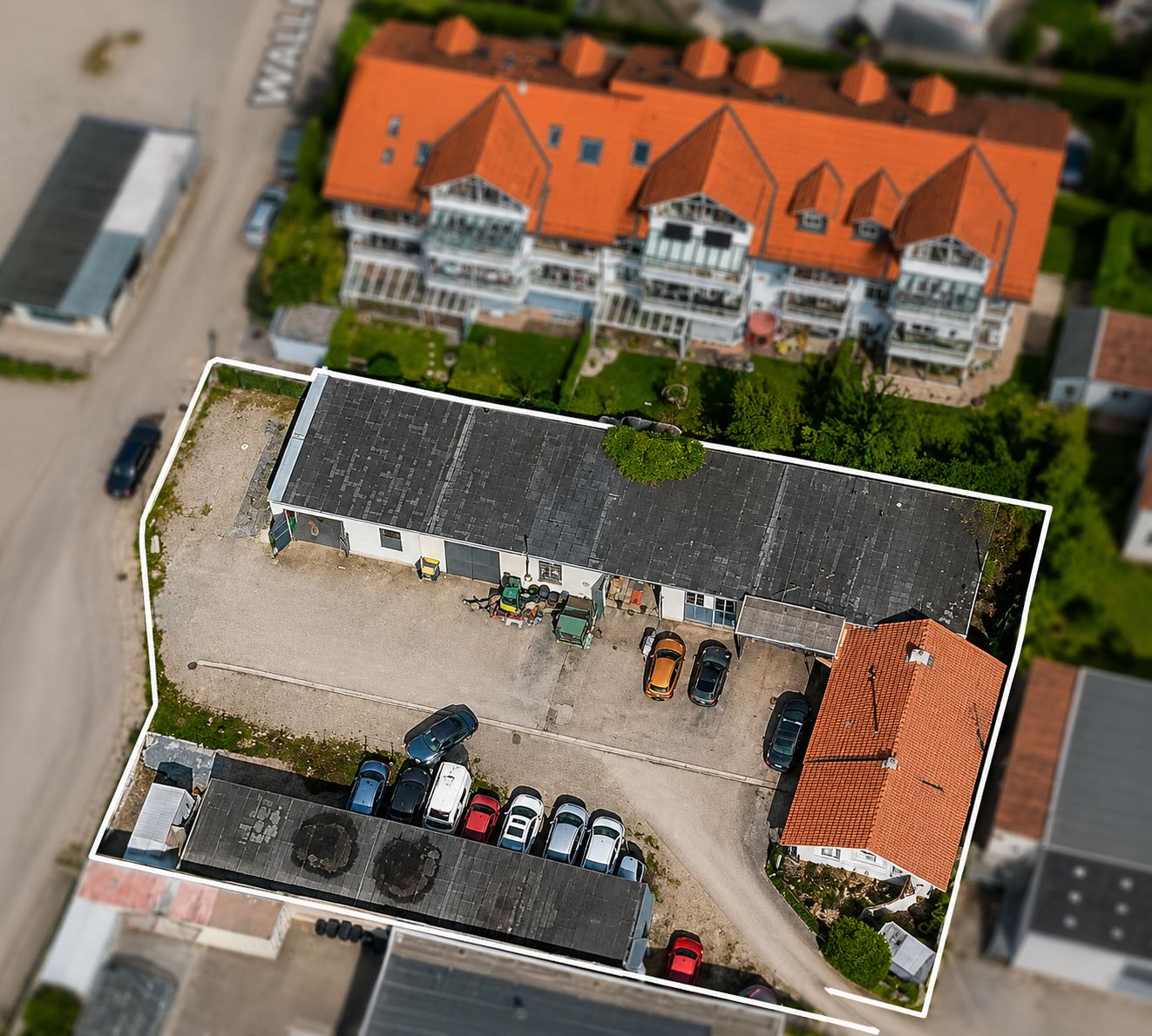 Luftbild eines umzäunten Grundstücks mit mehreren Häusern, Parkplätzen und Fahrzeugen.