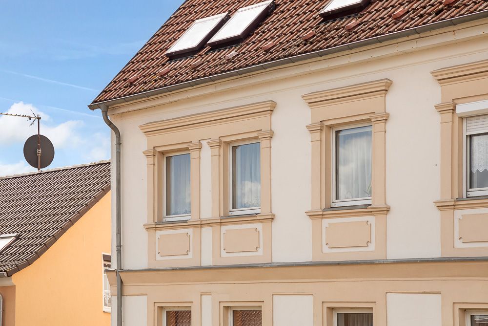 Vorderseite eines hellen Wohnhauses mit Satteldach und mehreren Fenstern.