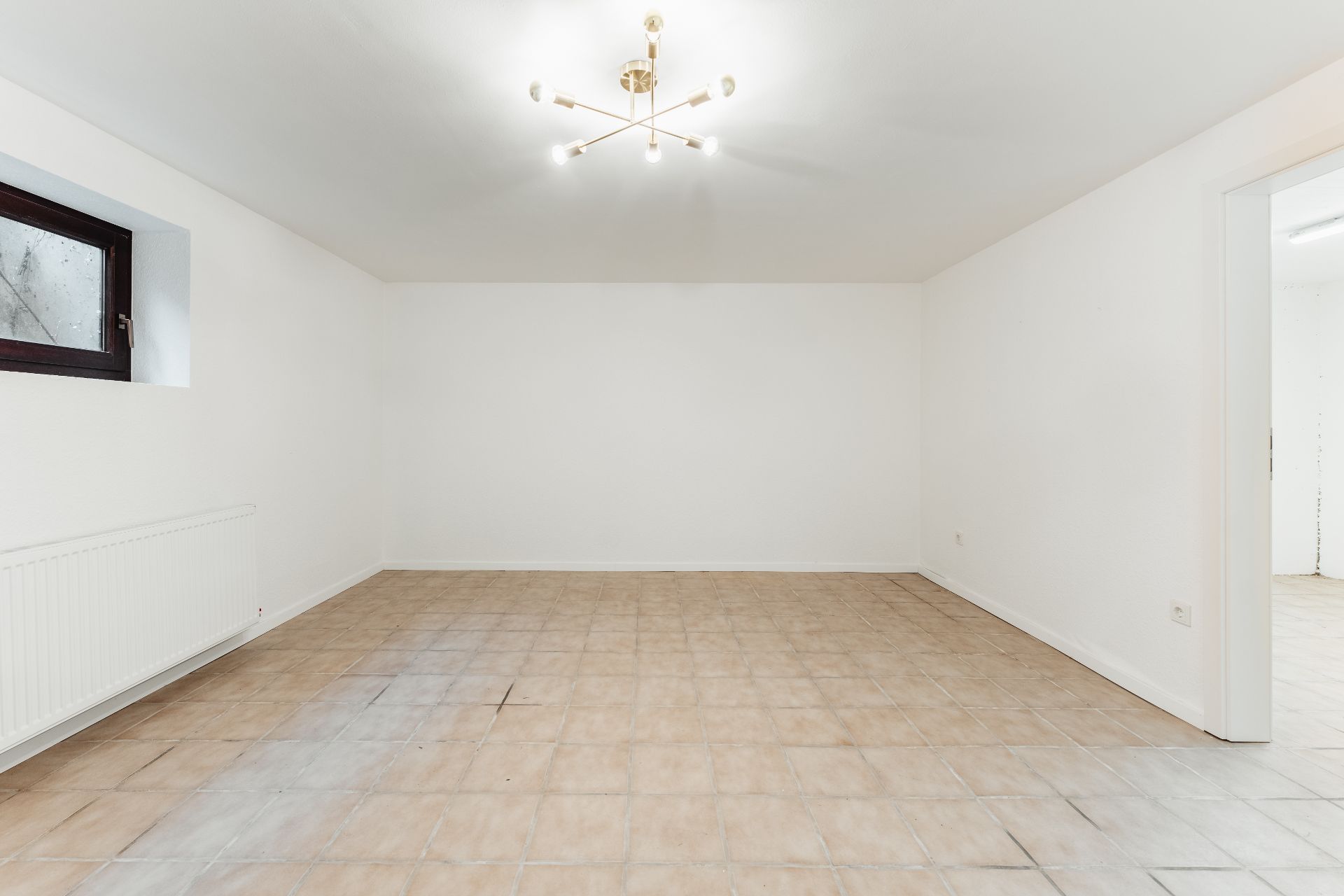 Leerer Raum mit Fliesenboden, weiß gestrichenen Wänden und moderner Deckenleuchte.