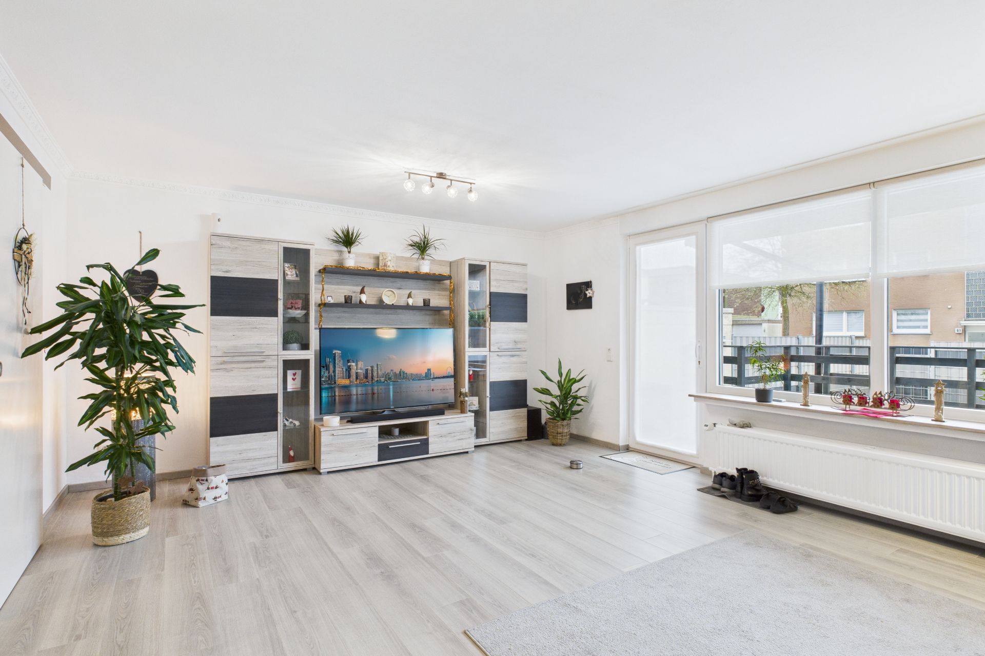 Helles Wohnzimmer mit TV-Schrank, Pflanzen und großen Fenstern zur Terrasse.