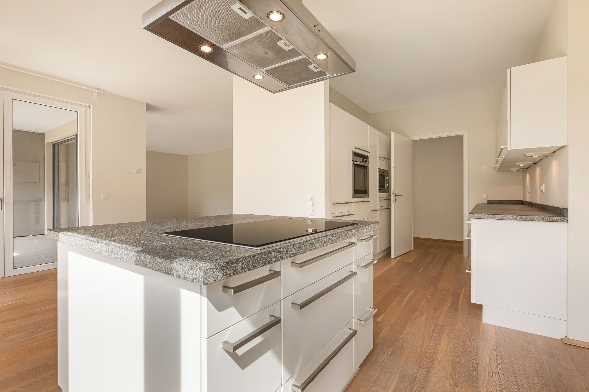Moderne, helle Einbauküche mit Kochinsel und weißen Schränken auf Holzfußboden.