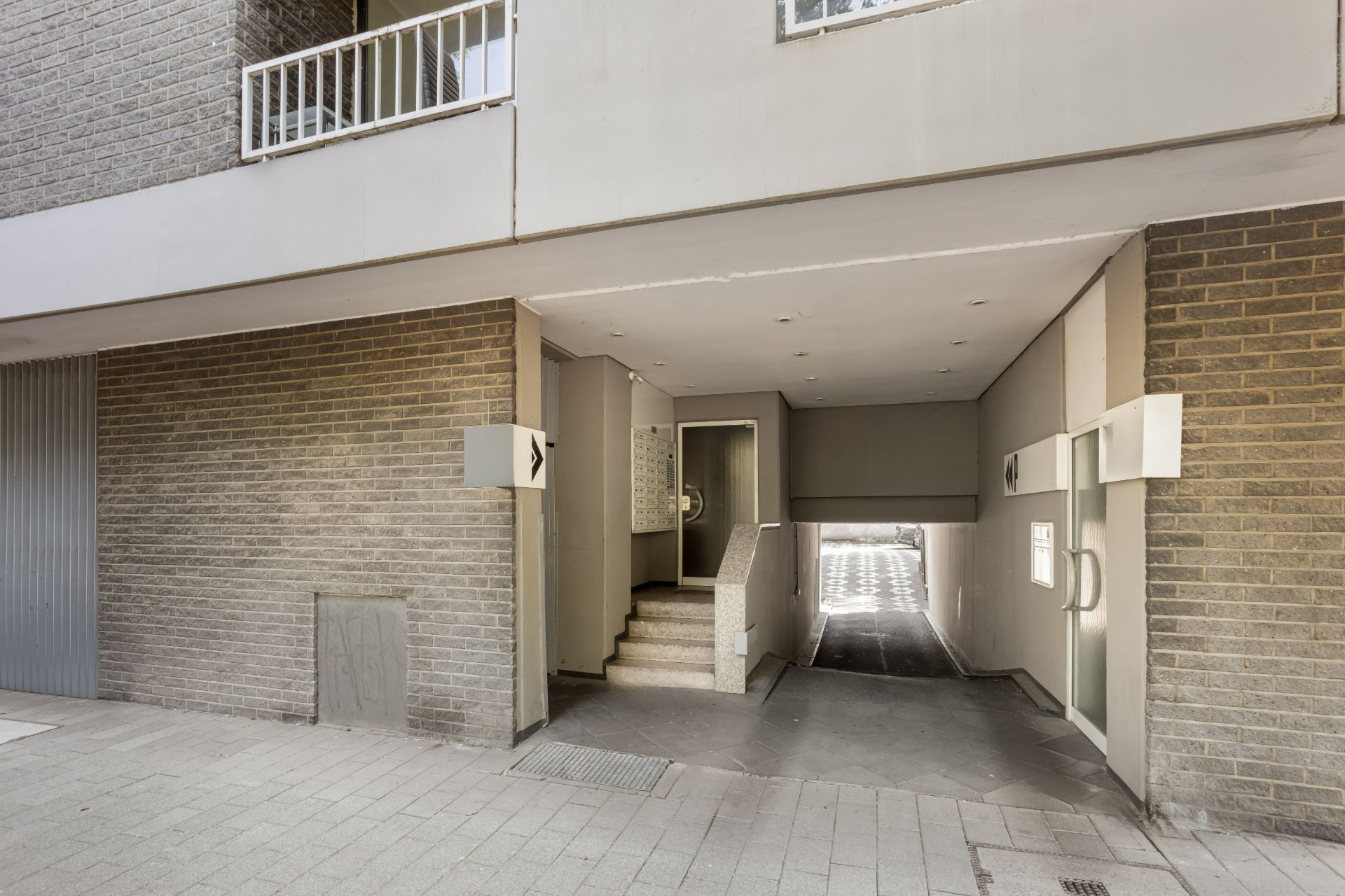 Eingang mit überdachtem Durchgang, Treppe und Zufahrt zu einer Tiefgarage an einem Wohnhaus.
