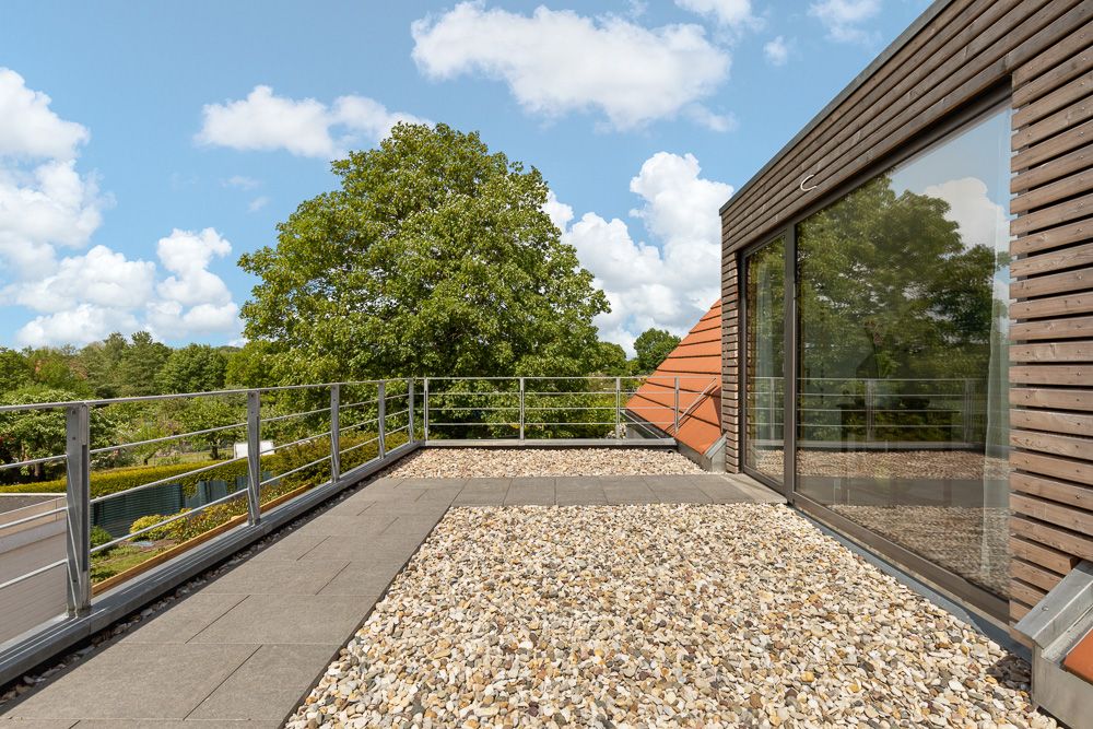 Dachterrasse mit Kiesbelag, Geländer und Blick auf Bäume, angrenzend an ein modernes Wohnhaus.