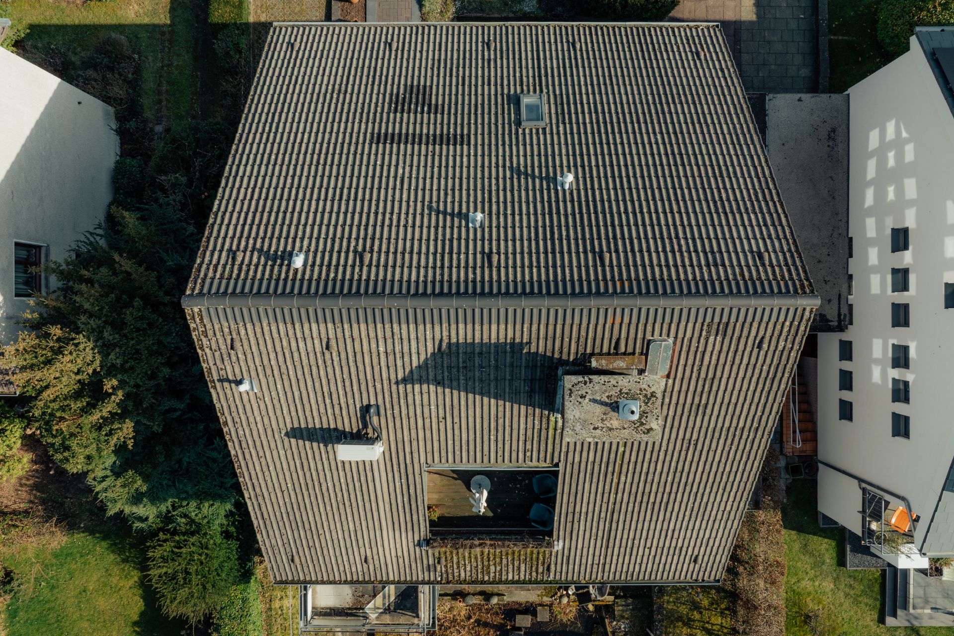 Luftaufnahme eines Hauses mit grauem Satteldach, mehreren Lüftungsrohren und Gartenflächen drumherum.