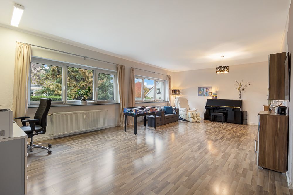Großes, helles Wohnzimmer mit Schreibtisch, Sofa, Klavier und großen Fenstern.