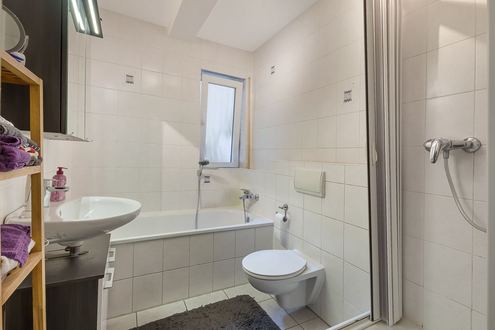 Modernes Badezimmer mit Badewanne, Waschbecken, WC und Regalen mit Handtüchern.