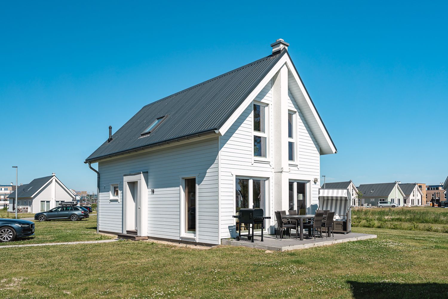 Weißes Einfamilienhaus mit Terrasse, Gartenmöbeln und Grill auf einer Wiese.
