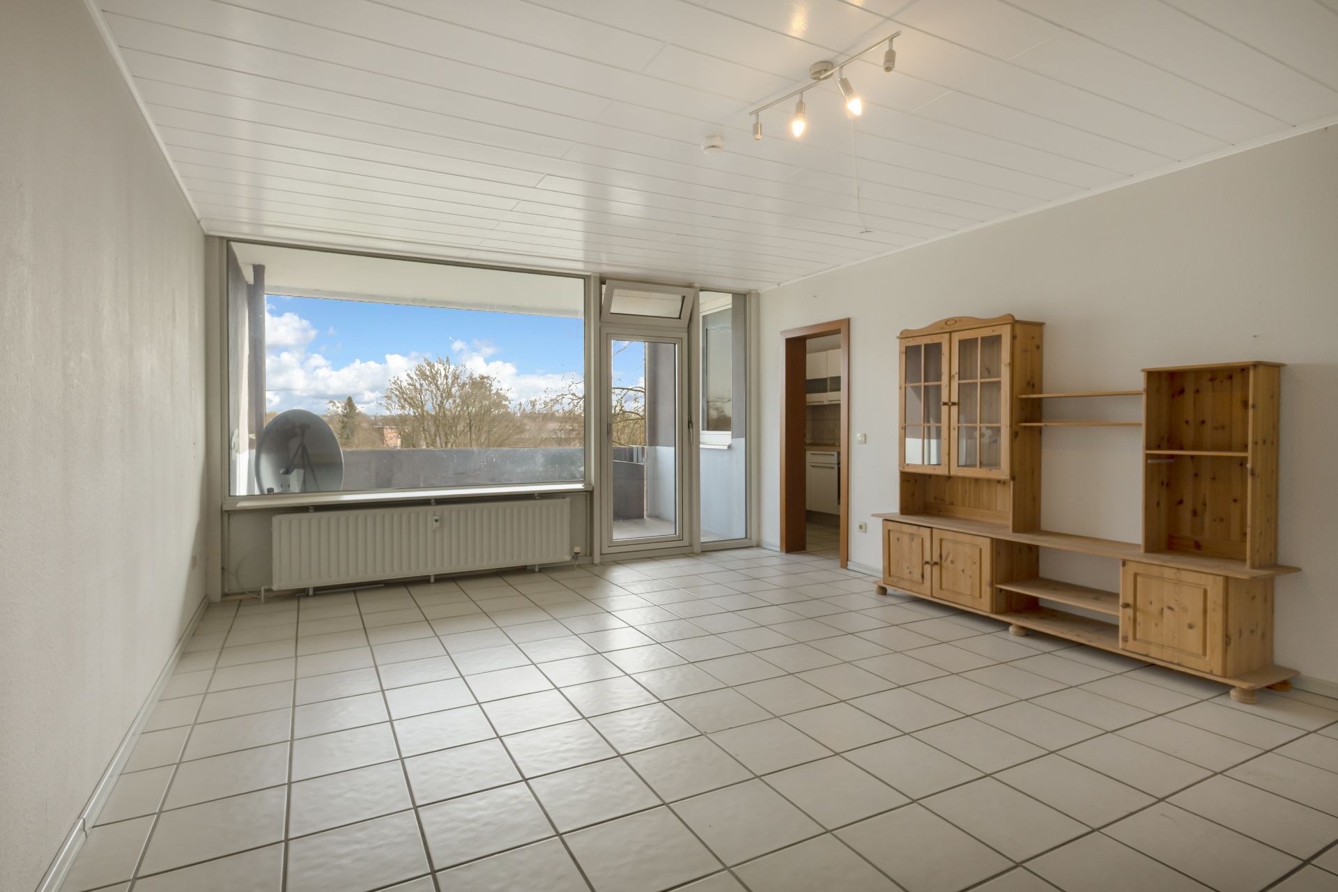 Helles Wohnzimmer mit Fliesenboden, Holzmöbeln und Zugang zu einem Balkon.