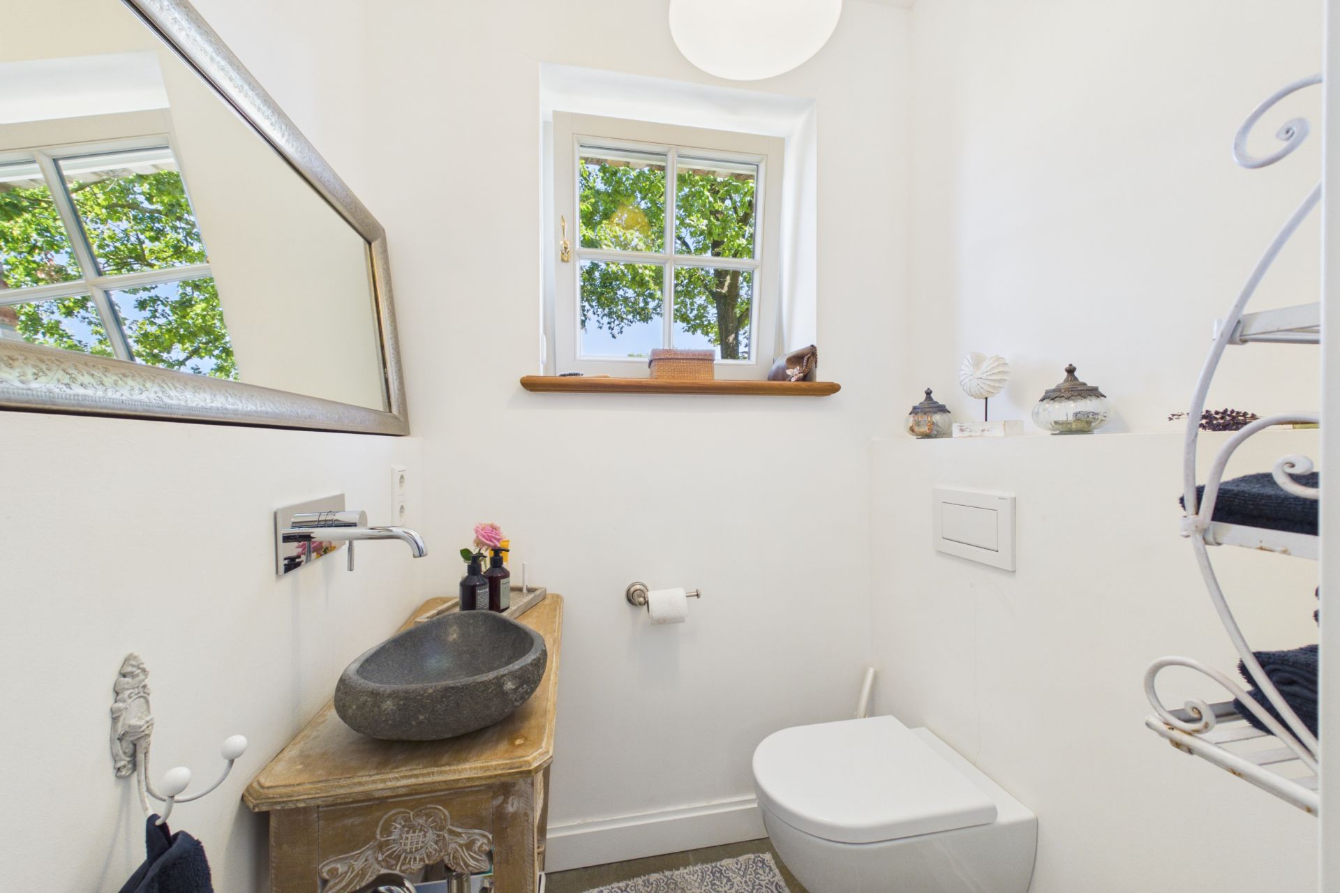 Kleines Bad mit Fenster, Wandtoilette, rundem Steinwaschbecken und Spiegel.