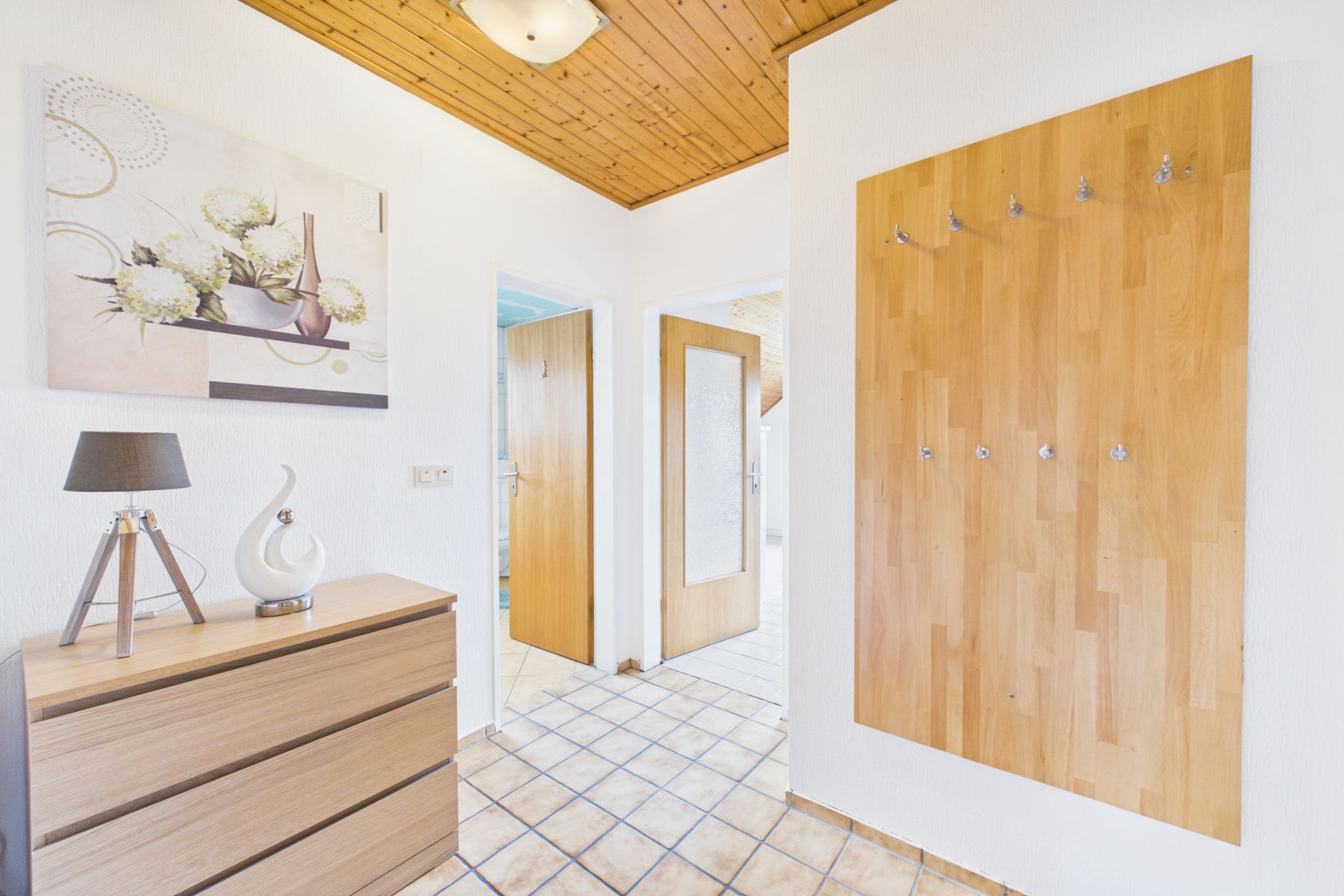 Heller Flur mit Holzgarderobe, Kommode, Lampe und Bild an der Wand.