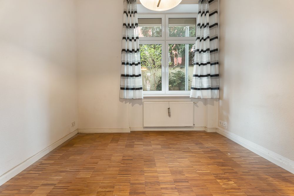 Leerer Raum mit Parkettboden, weißem Fenster, gestreiften Vorhängen und einer Deckenlampe.