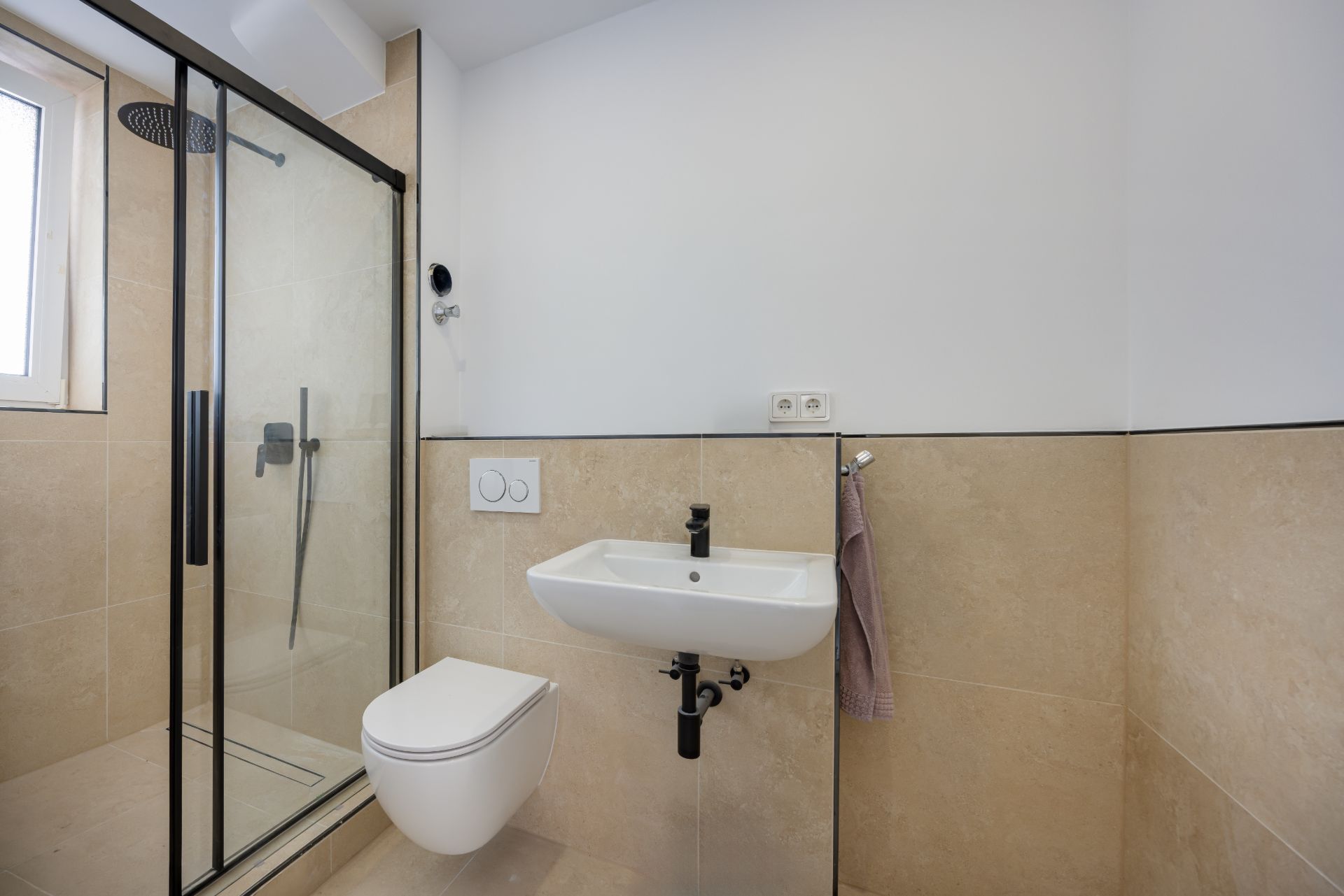 Modernes Badezimmer mit Dusche, WC und kleinem Waschbecken an beige gefliester Wand.