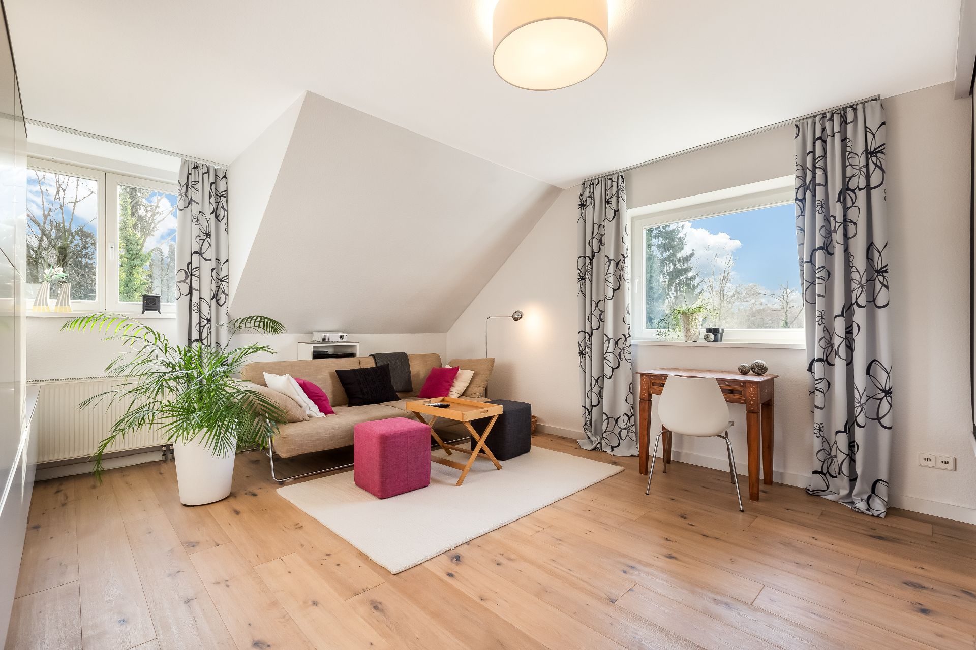 Helles Wohnzimmer mit Sofa, Tisch, Schreibtisch, Stuhl und Pflanzen, Holzfußboden.