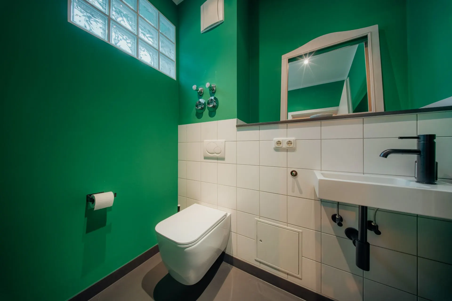 Kleines Badezimmer mit grünen Wänden, Wandtoilette, Waschbecken und Spiegel.
