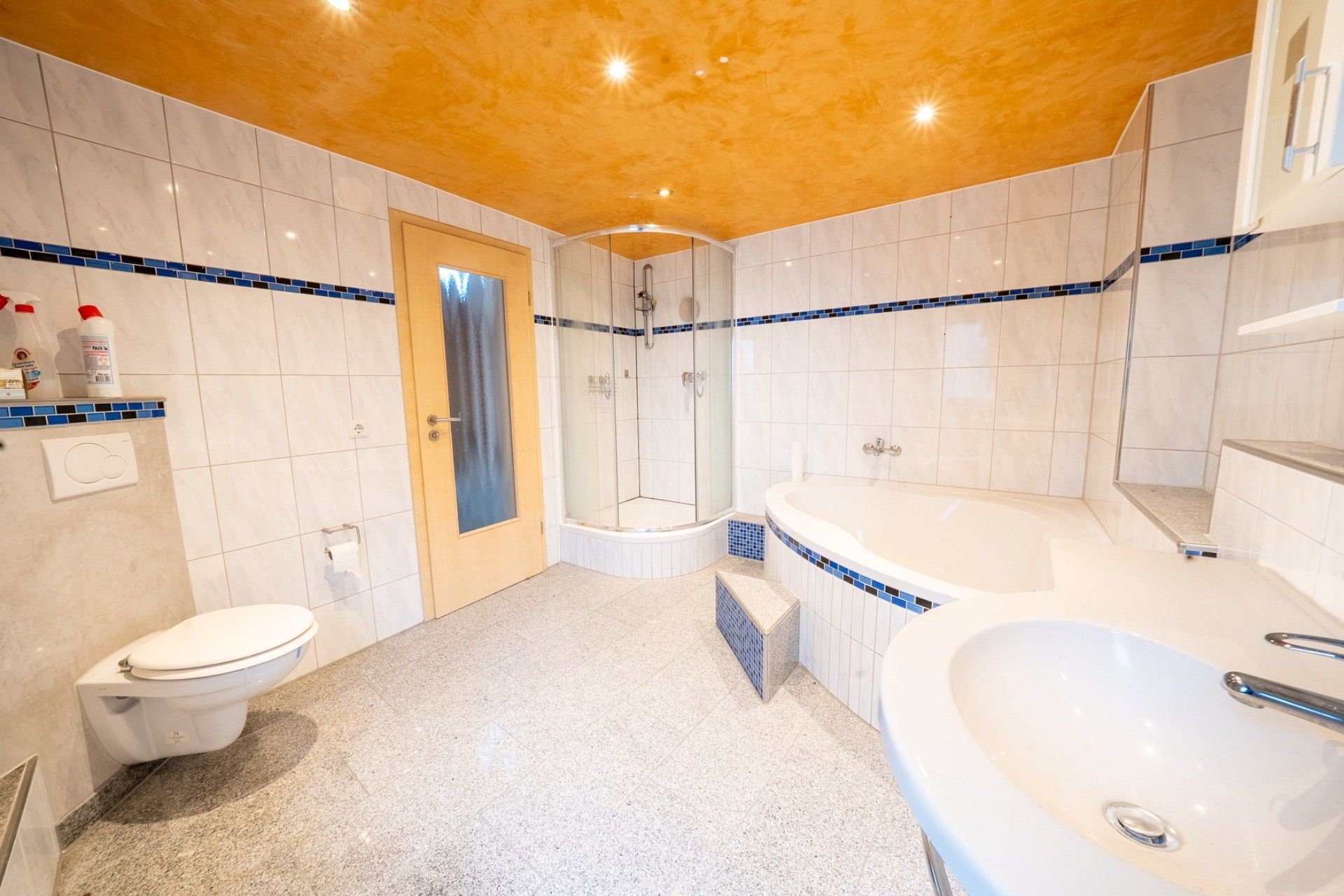 Helles Bad mit Dusche, Badewanne, Waschbecken und WC, gefliest, mit gelber Decke.