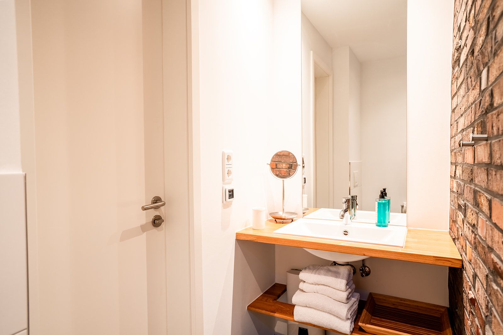 Modernes Badezimmer mit Waschbecken, Spiegel und Handtüchern auf einem Holzregal.
