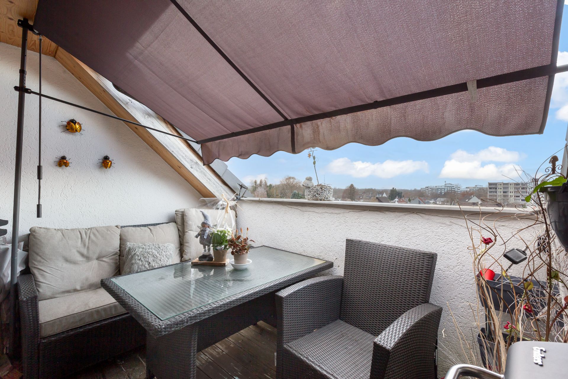 Balkon mit Markise, Sitzgruppe, Glastisch und Pflanzen. Im Hintergrund Blick auf die Stadt.